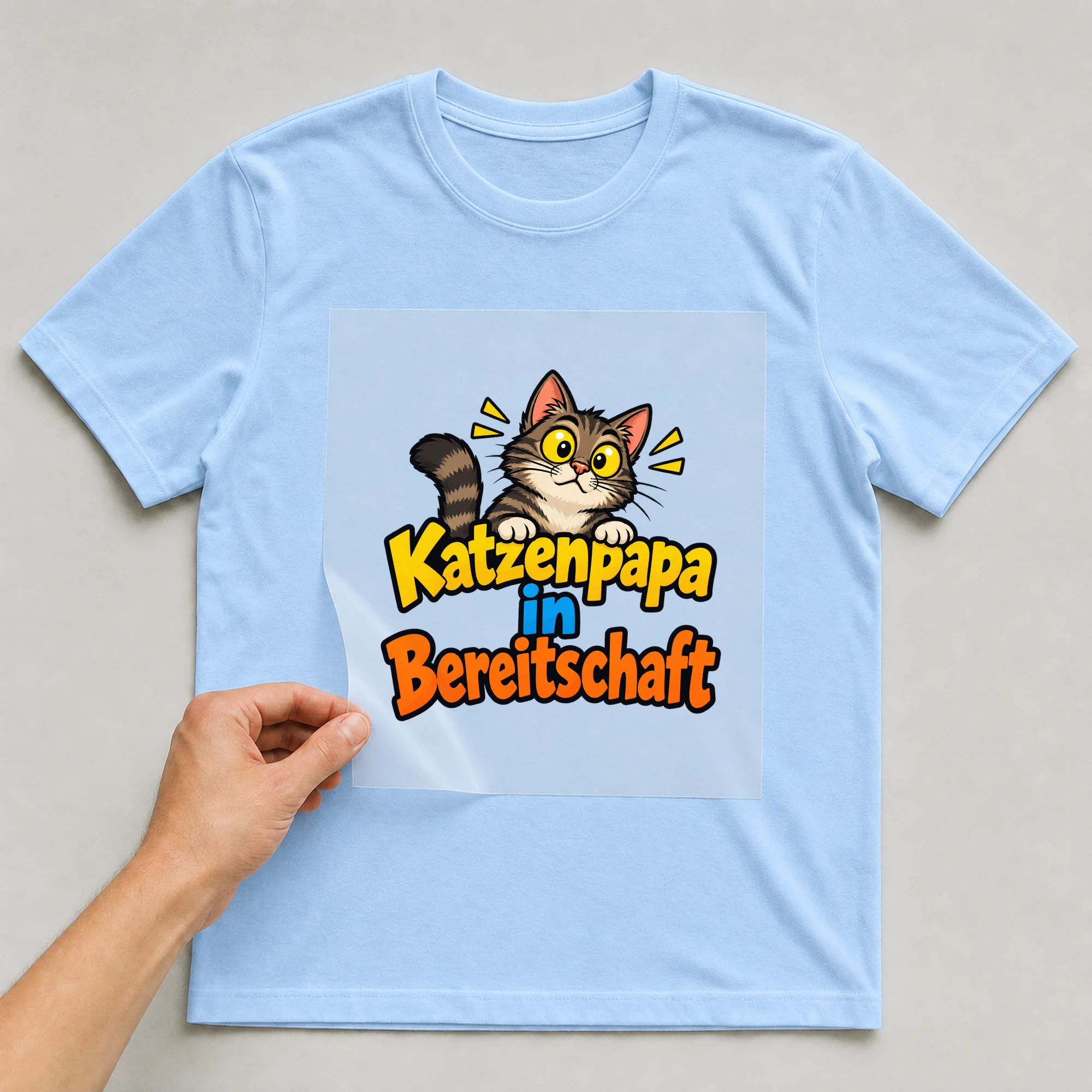 Bügelbild „Katzenpapa in Bereitschaft“ auf babyblauem T-Shirt, Folie wird aufgelegt