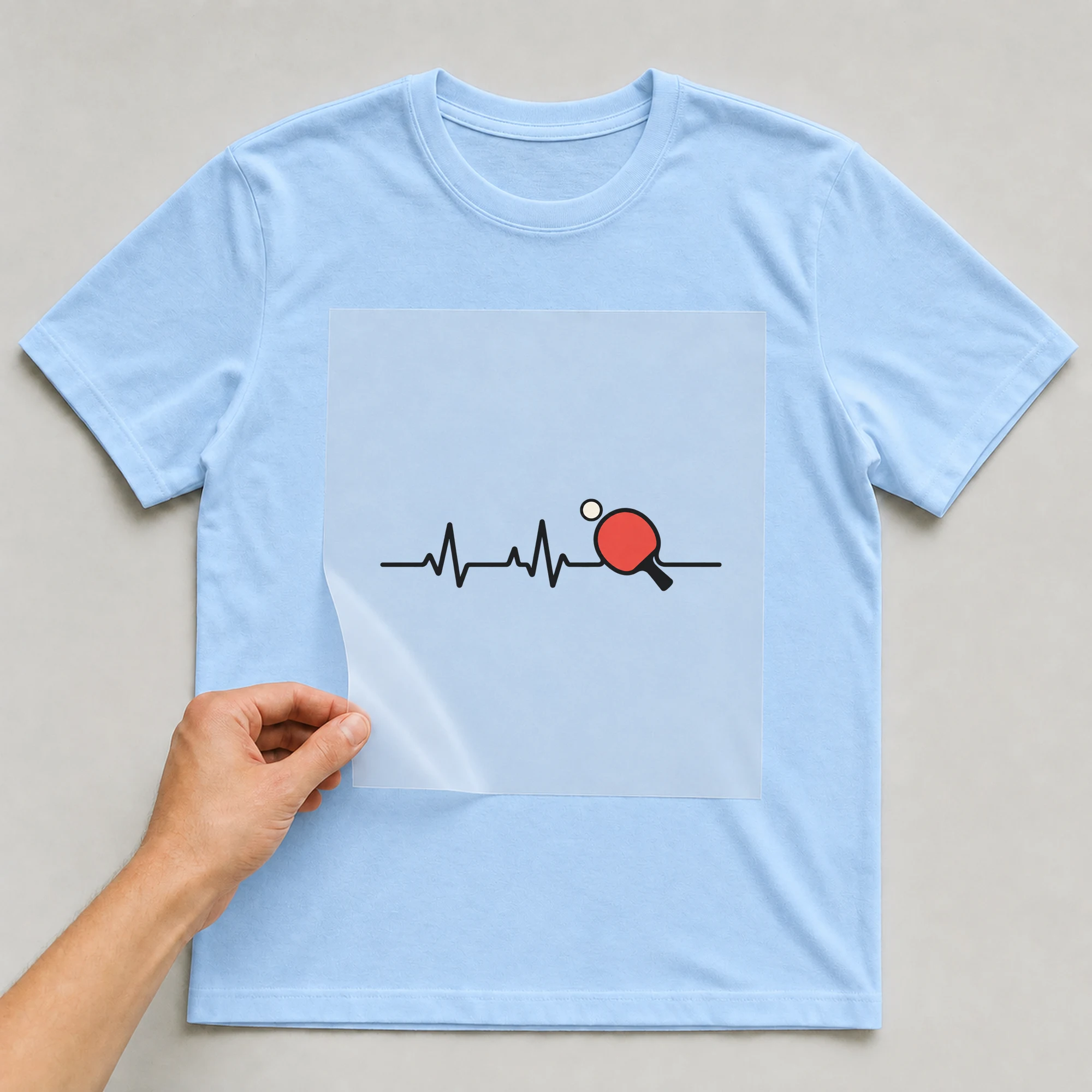 Bügelbild „Tischtennis Herzschlag“ auf babyblauem T-Shirt, Folie wird aufgelegt