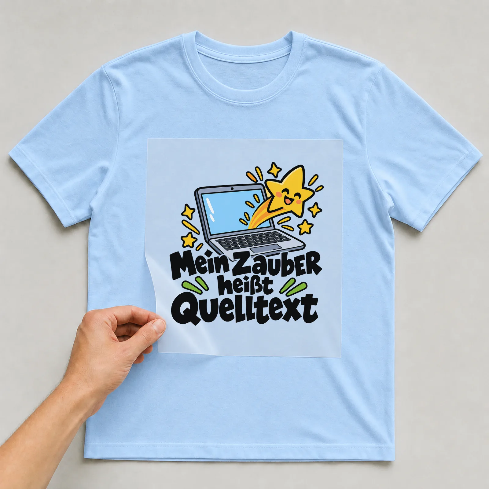 Bügelbild „Mein Zauber heißt Quelltext“ auf hellblauem T-Shirt, Folie wird aufgelegt