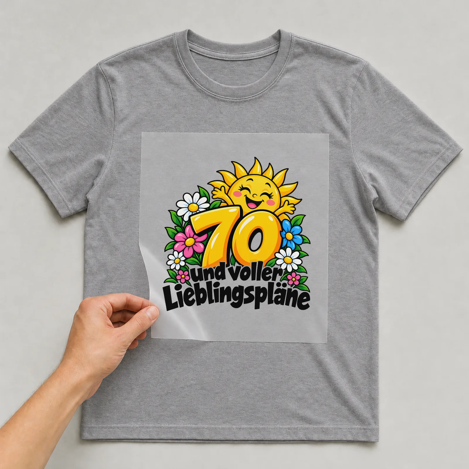 Bügelbild „70 und voller Lieblingspläne“ auf grauem T-Shirt, Folie wird aufgelegt