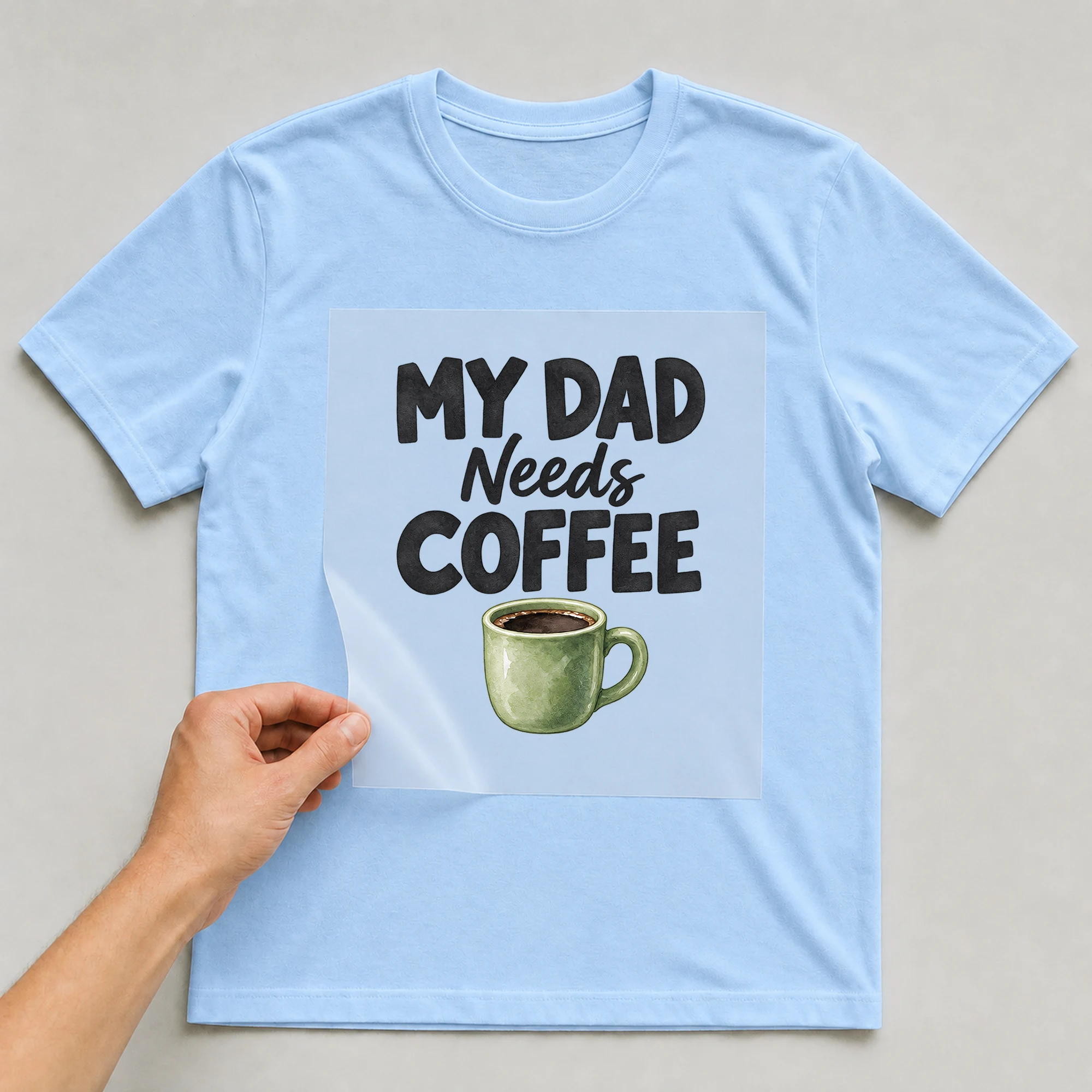 Bügelbild „My Dad Needs Coffee“ auf babyblauem T-Shirt, Folie wird aufgelegt