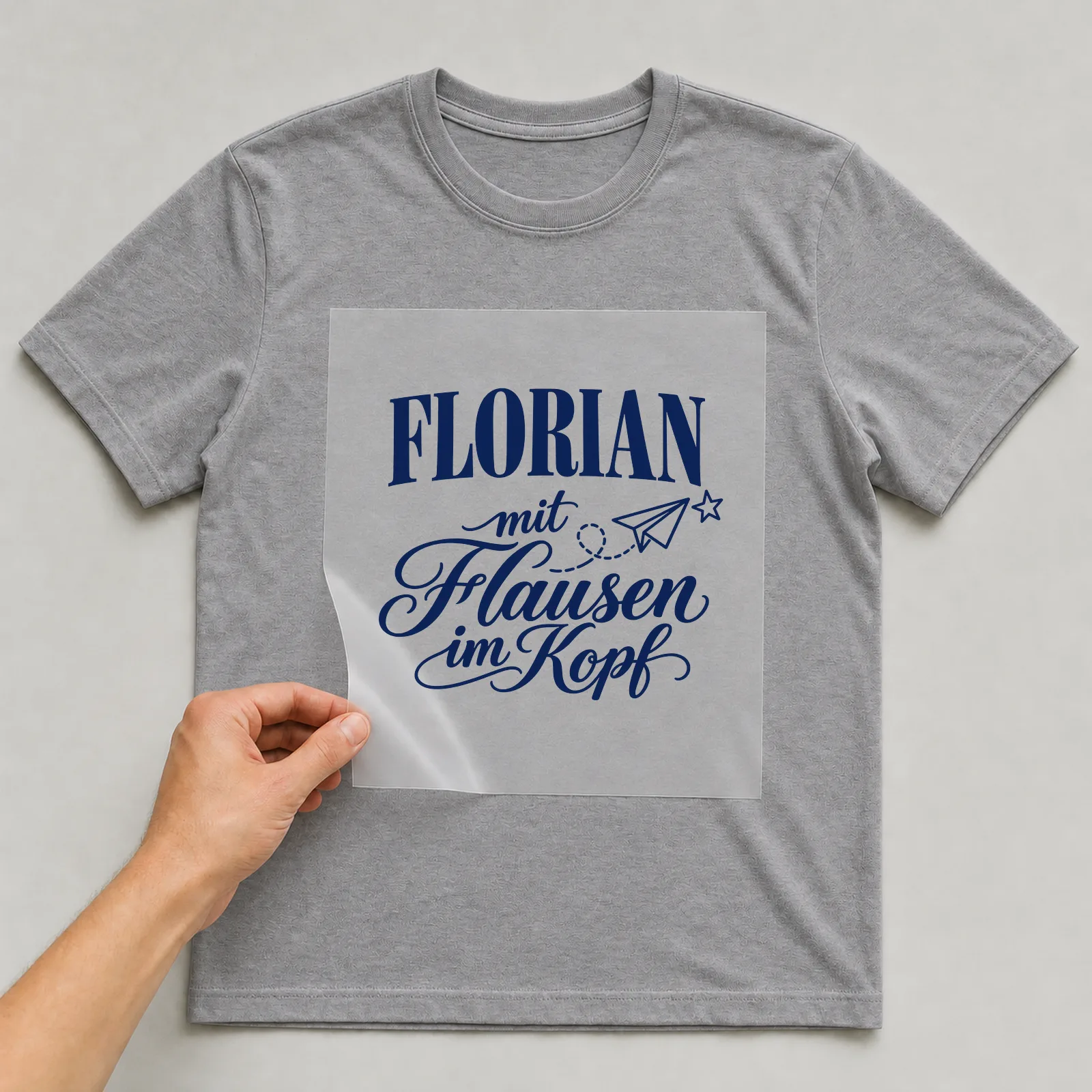 Bügelbild „Florian mit Flausen im Kopf“ auf grauem T-Shirt, Folie wird aufgelegt