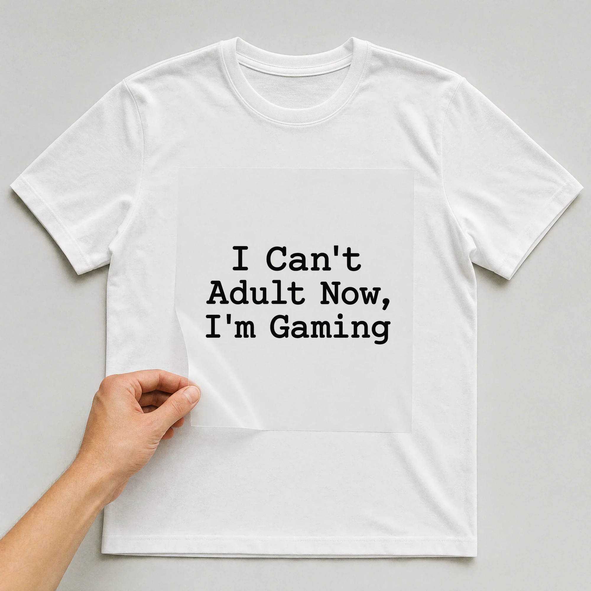 Bügelbild „I Can't Adult Now, I'm Gaming“ auf weißem T-Shirt, Folie wird aufgelegt