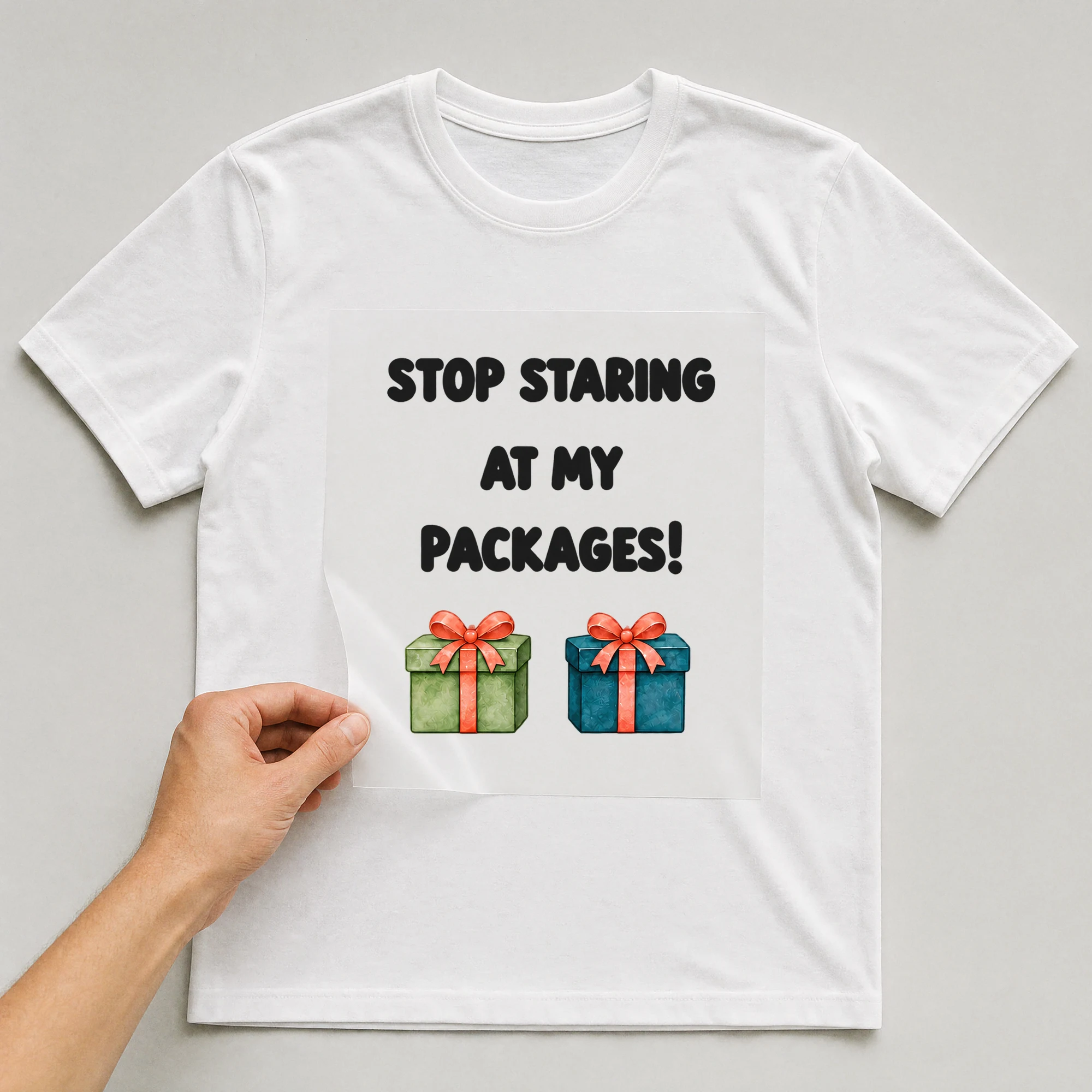 Bügelbild „STOP STARING AT MY PACKAGES!“ auf weißem T-Shirt, Folie wird aufgelegt