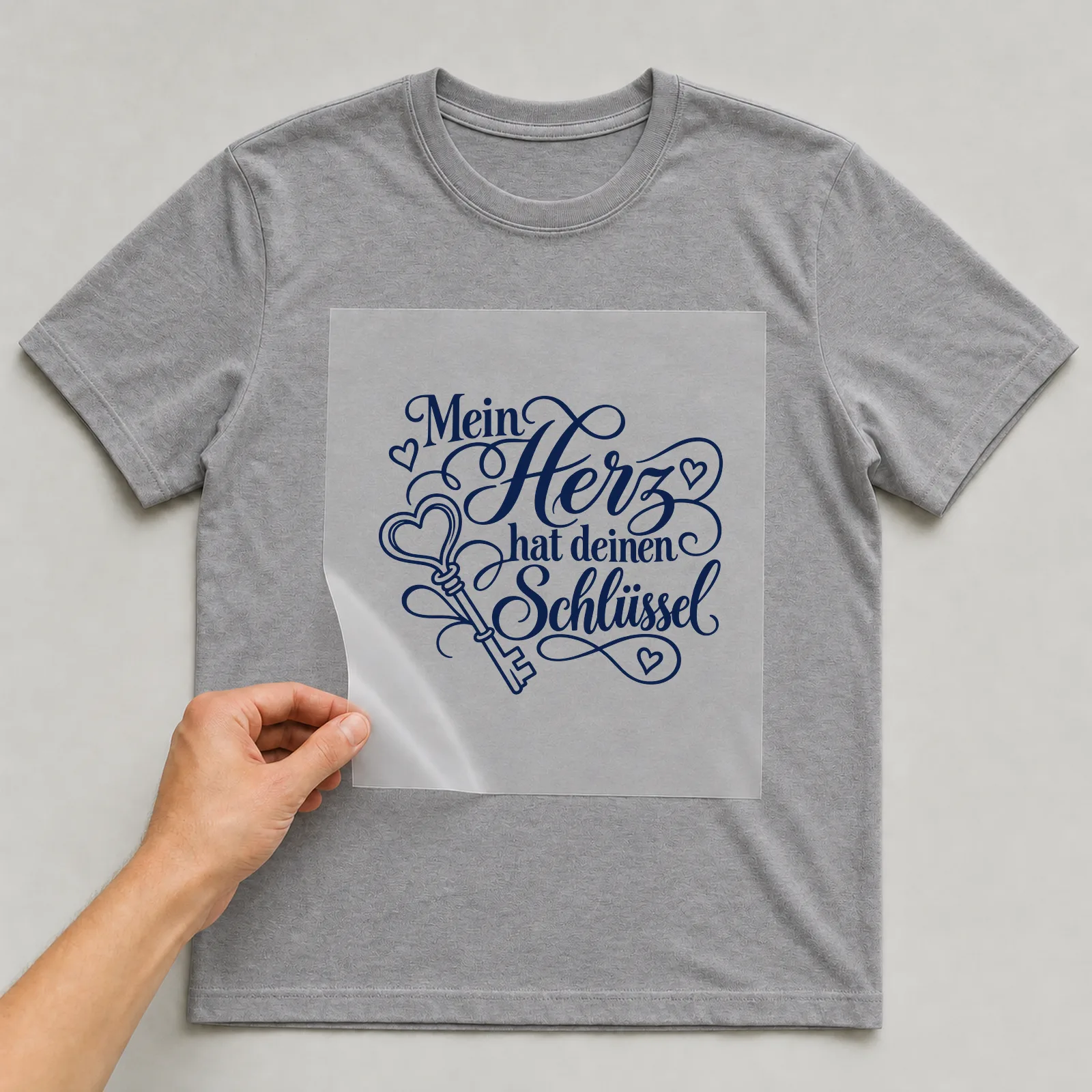 Bügelbild „Mein Herz hat deinen Schlüssel“ auf grauem T-Shirt, Folie wird aufgelegt