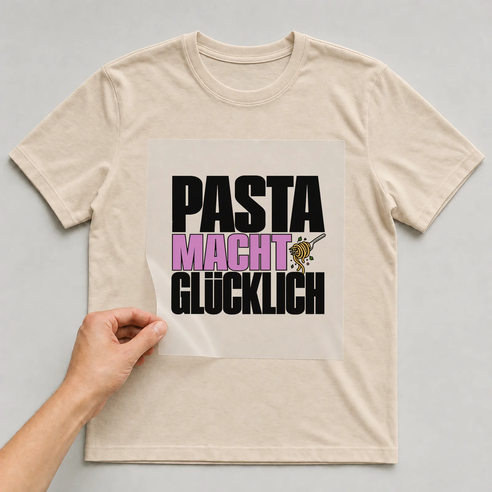 Bügelbild „Pasta macht glücklich“ (kompakter Plakatschrift) auf beigem T-Shirt, Folie wird aufgelegt