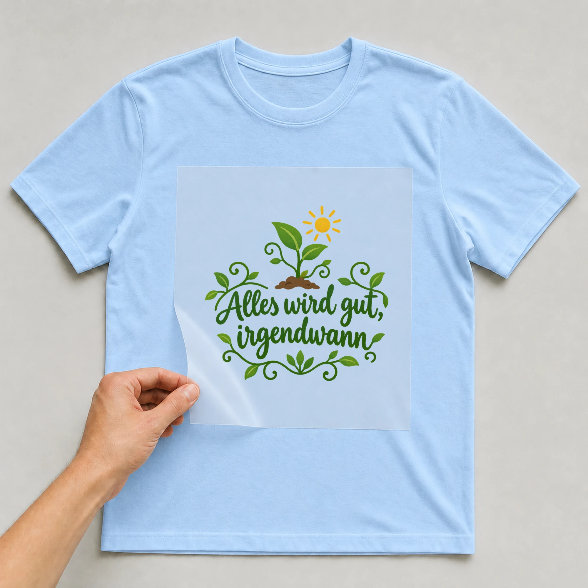 Bügelbild „Alles wird gut, irgendwann“ auf babyblauem T-Shirt, Folie wird aufgelegt