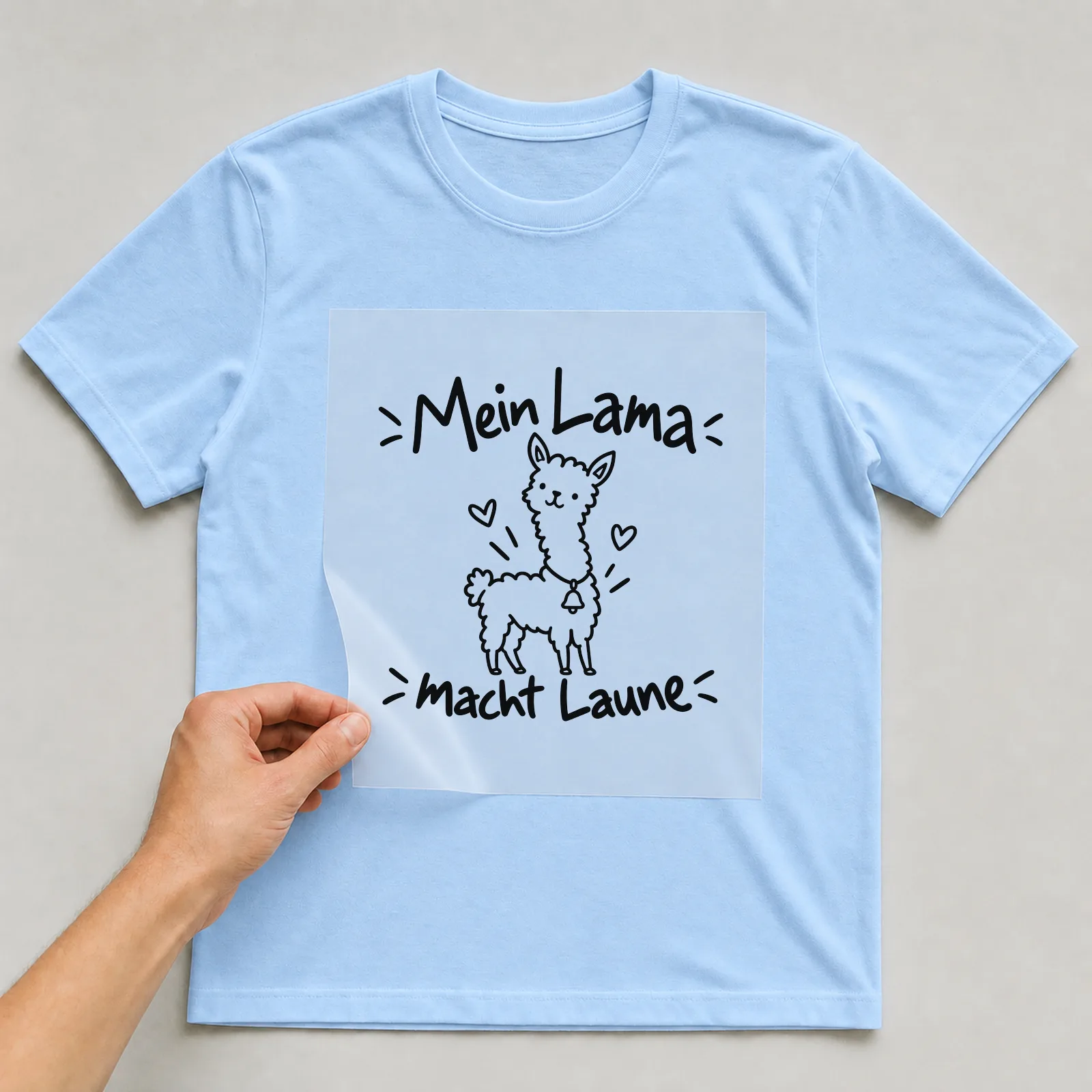 Bügelbild „Mein Lama macht Laune“ auf hellblauem T-Shirt, Folie wird aufgelegt