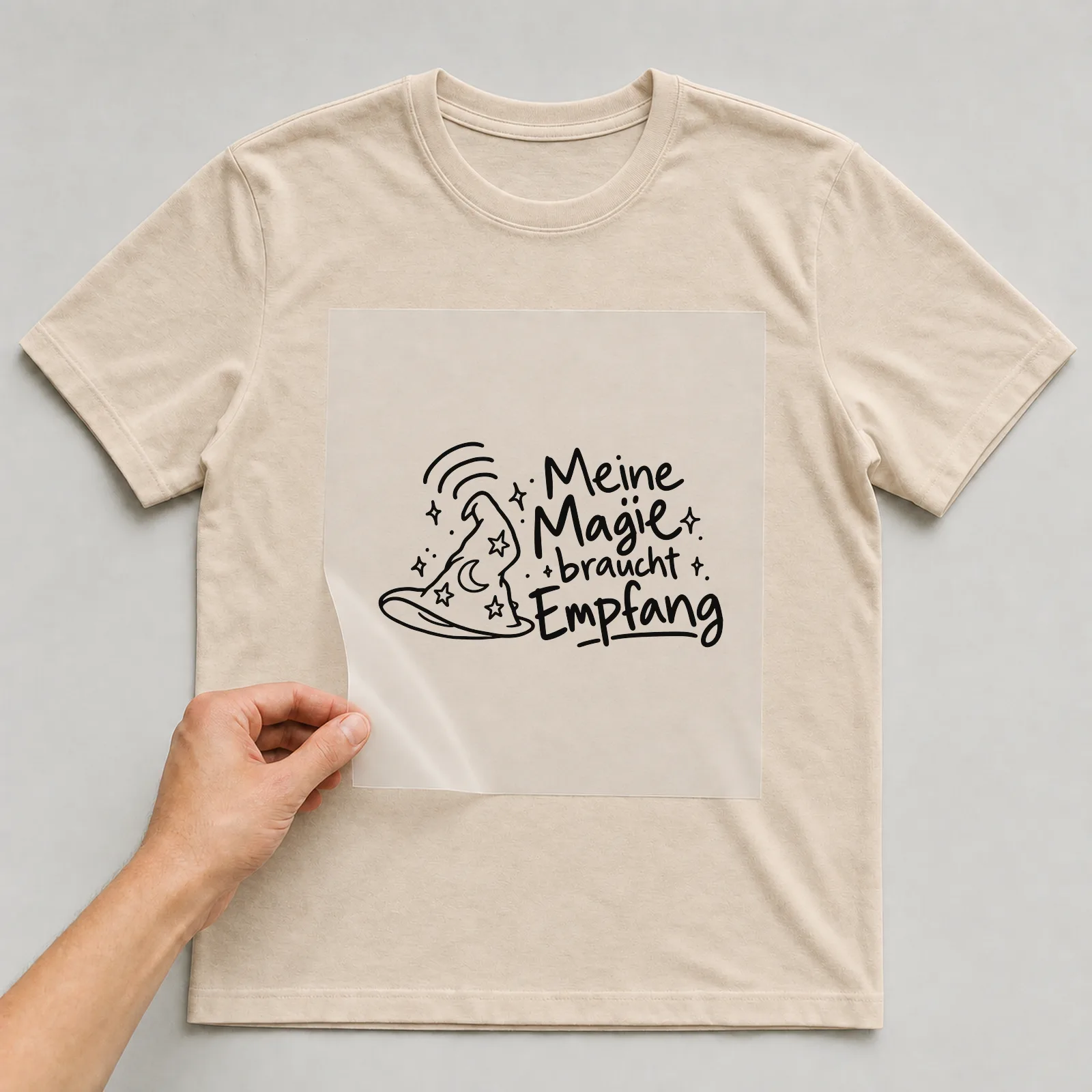 Bügelbild „Meine Magie braucht Empfang“ auf beigem T-Shirt, Folie wird aufgelegt