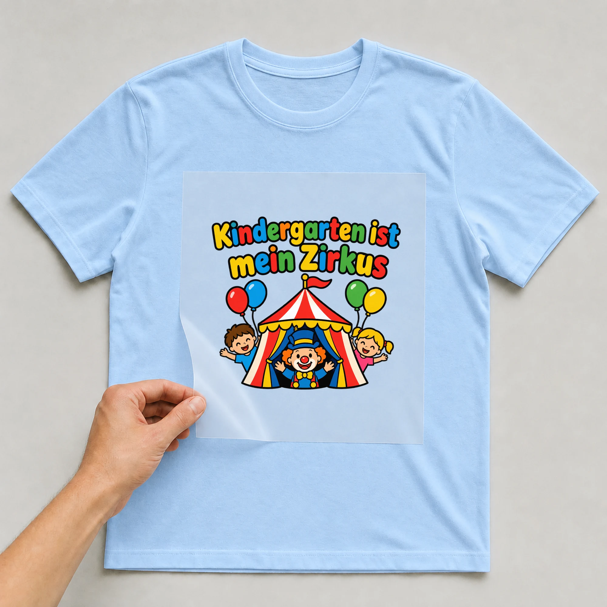 Bügelbild „Kindergarten ist mein Zirkus“ auf babyblauem T-Shirt, Folie wird aufgelegt