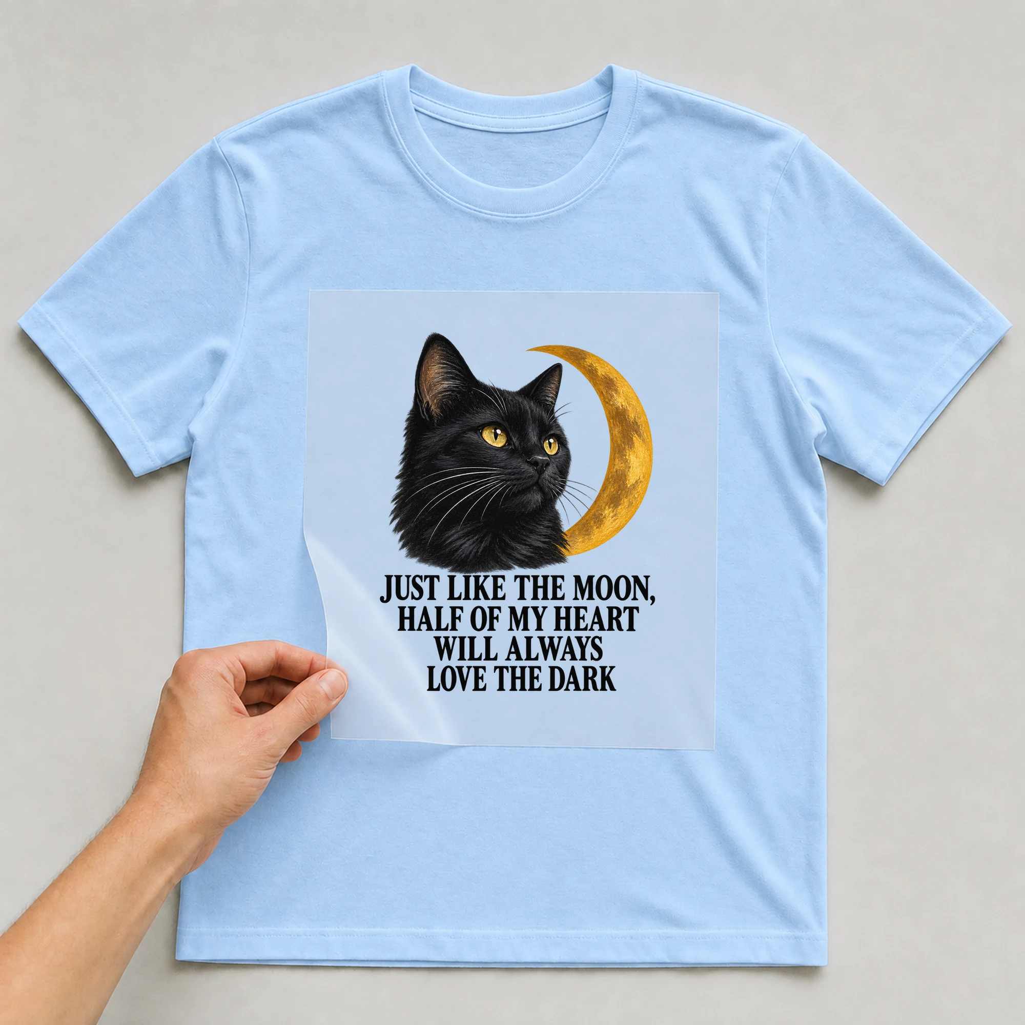 Bügelbild „Just Like The Moon, Half Of My Heart Will Always Love The Dark“ auf babyblauem T-Shirt, Folie wird aufgelegt