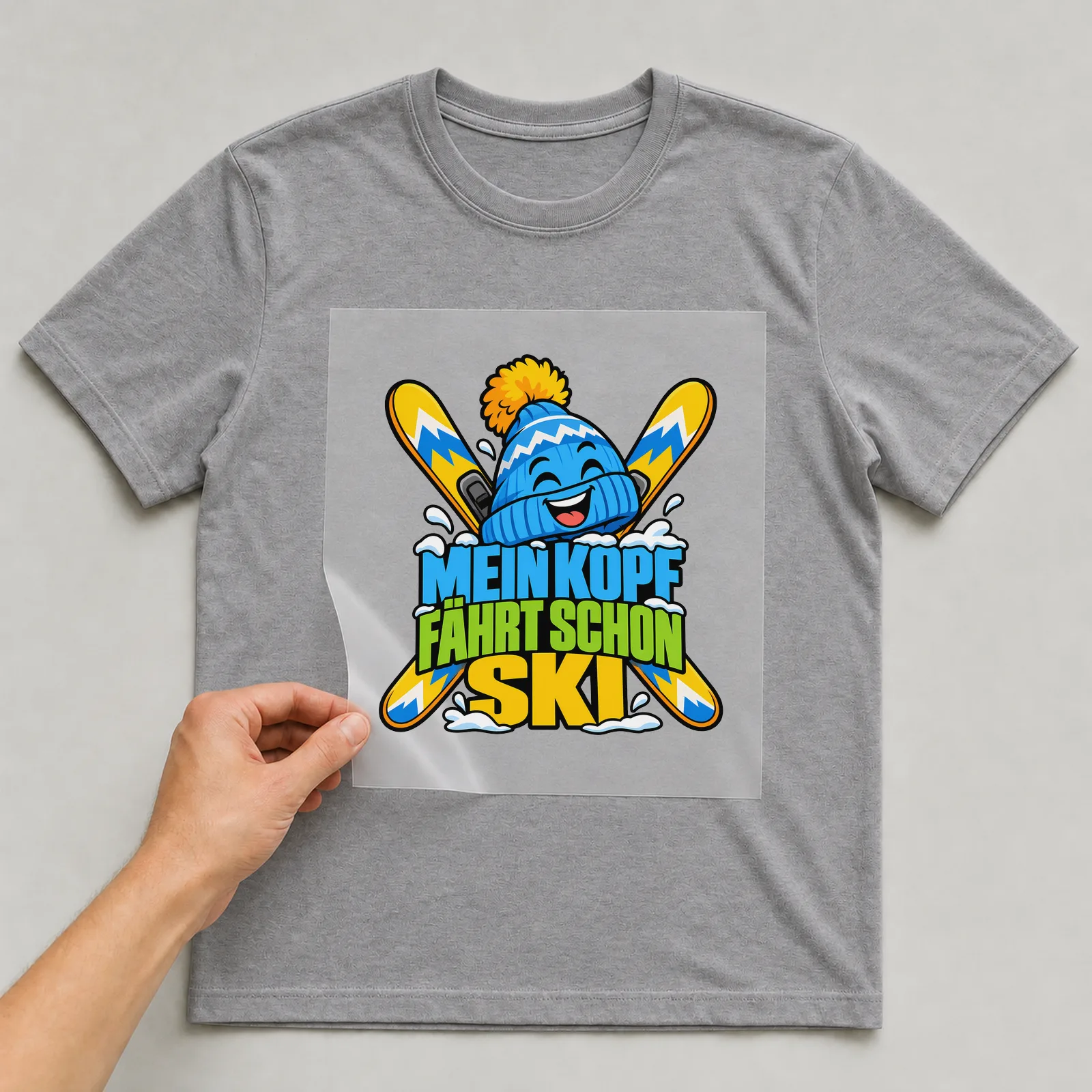 Bügelbild „Mein Kopf fährt schon Ski“ auf grauem T-Shirt, Folie wird aufgelegt