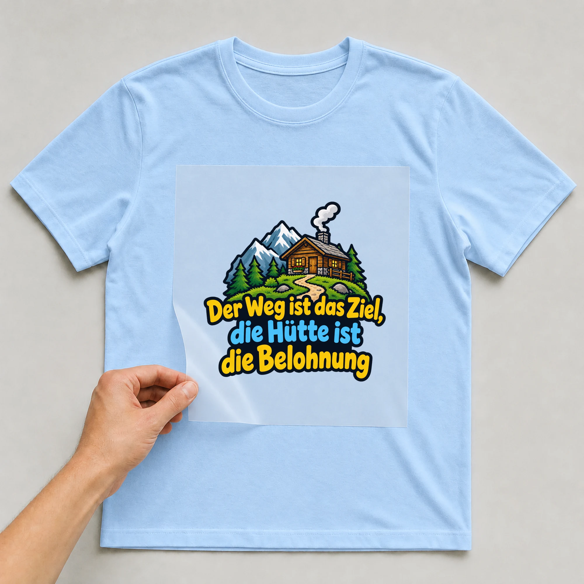 Bügelbild „Der weg ist das ziel die“ auf babyblauem T-Shirt, Folie wird aufgelegt
