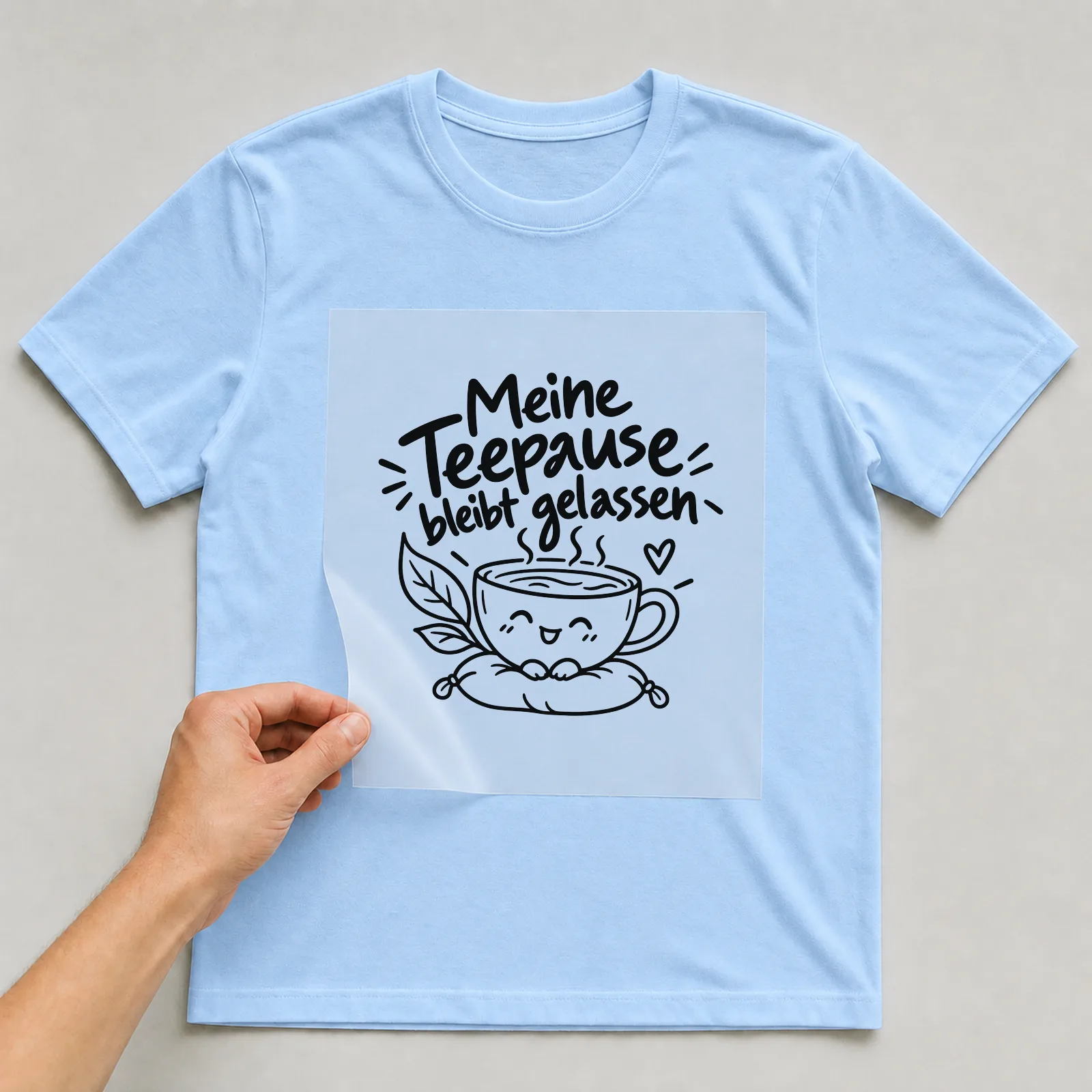 Bügelbild „Meine Teepause bleibt gelassen“ auf hellblauem T-Shirt, Folie wird aufgelegt