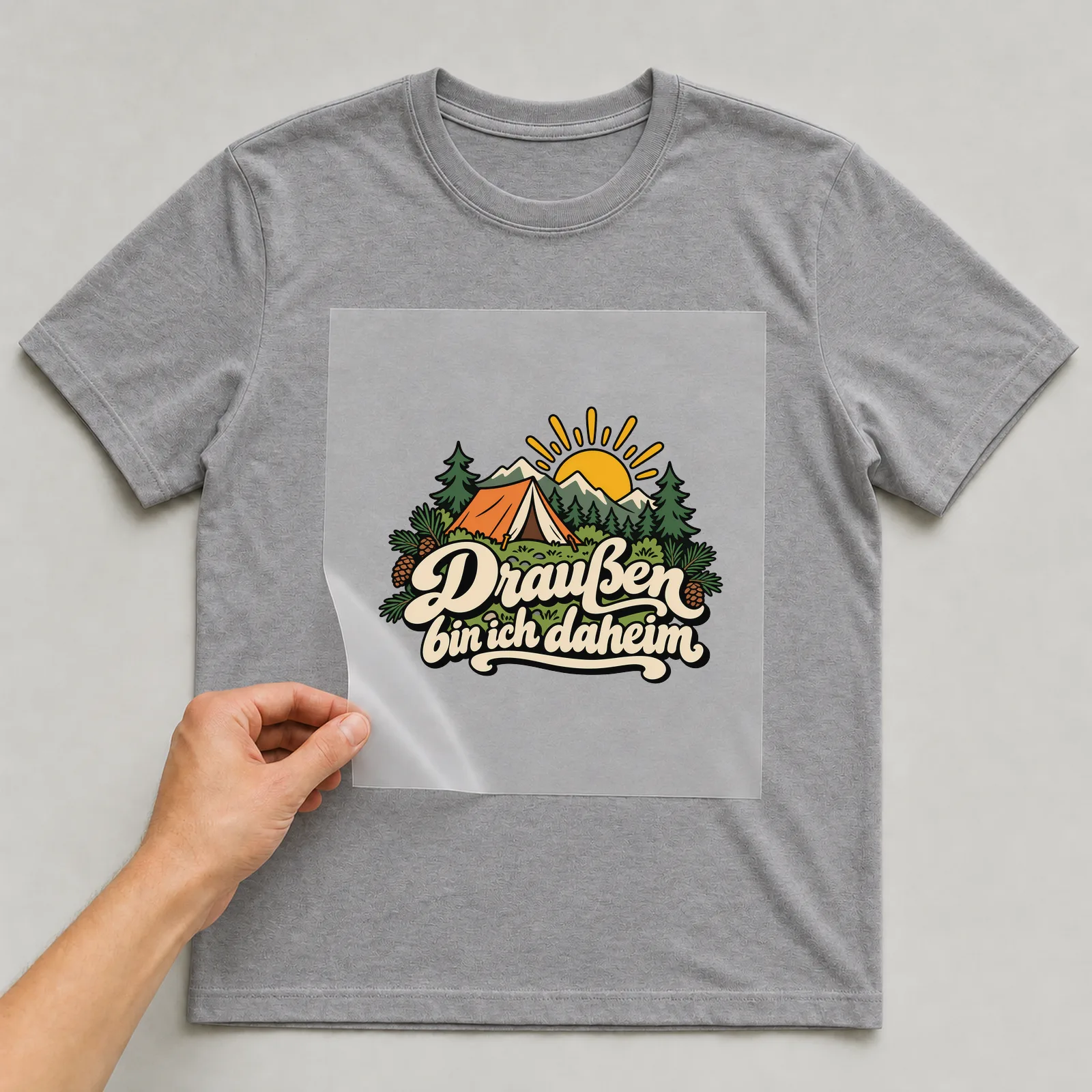 Bügelbild „Draußen bin ich daheim“ auf grauem T-Shirt, Folie wird aufgelegt