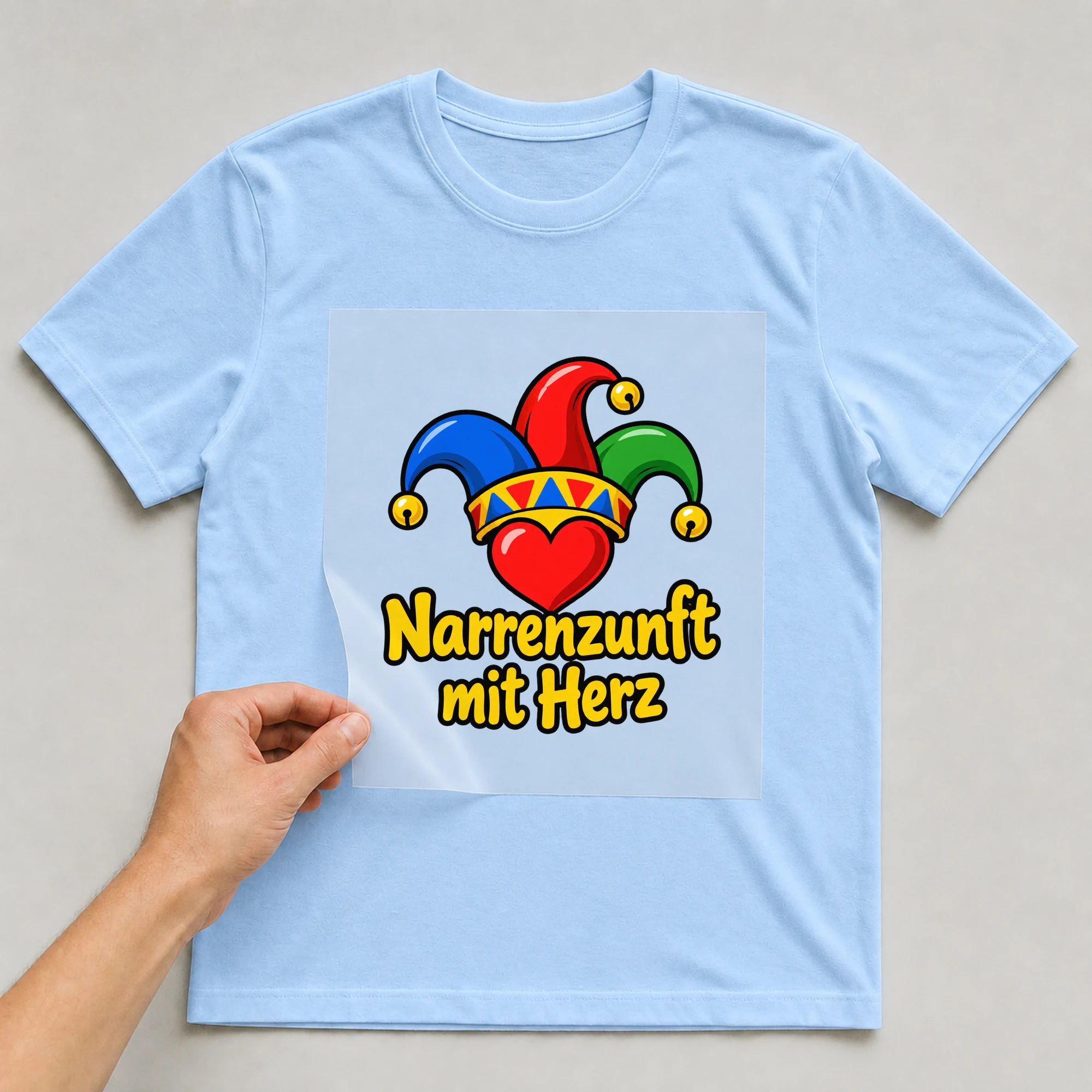 Bügelbild „Narrenzunft mit Herz“ auf babyblauem T-Shirt, Folie wird aufgelegt