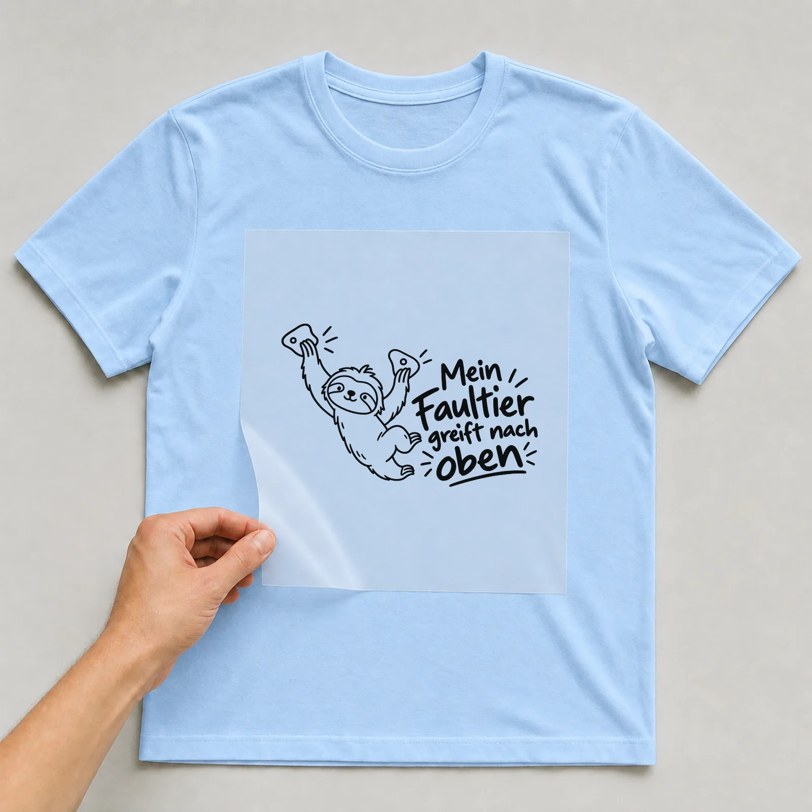 Bügelbild „Mein Faultier greift nach oben“ auf hellblauem T-Shirt, Folie wird aufgelegt