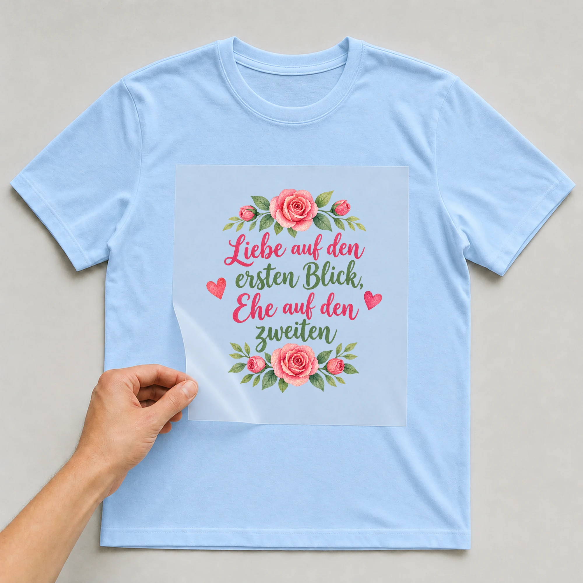 Bügelbild „Liebe auf den ersten Blick, Ehe auf den zweiten“ auf babyblauem T-Shirt, Folie wird aufgelegt