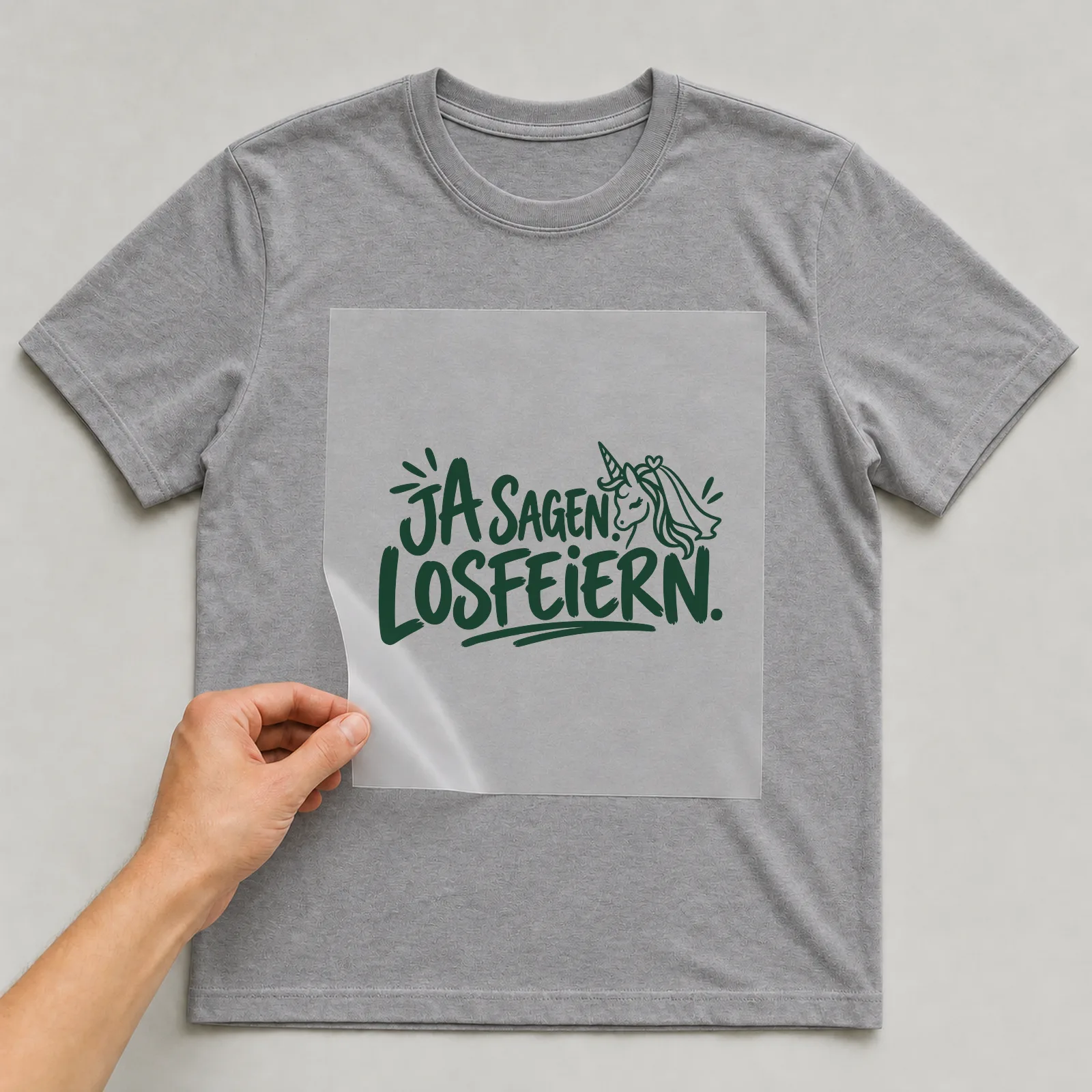 Bügelbild „Ja sagen. Losfeiern.“ auf grauem T-Shirt, Folie wird aufgelegt