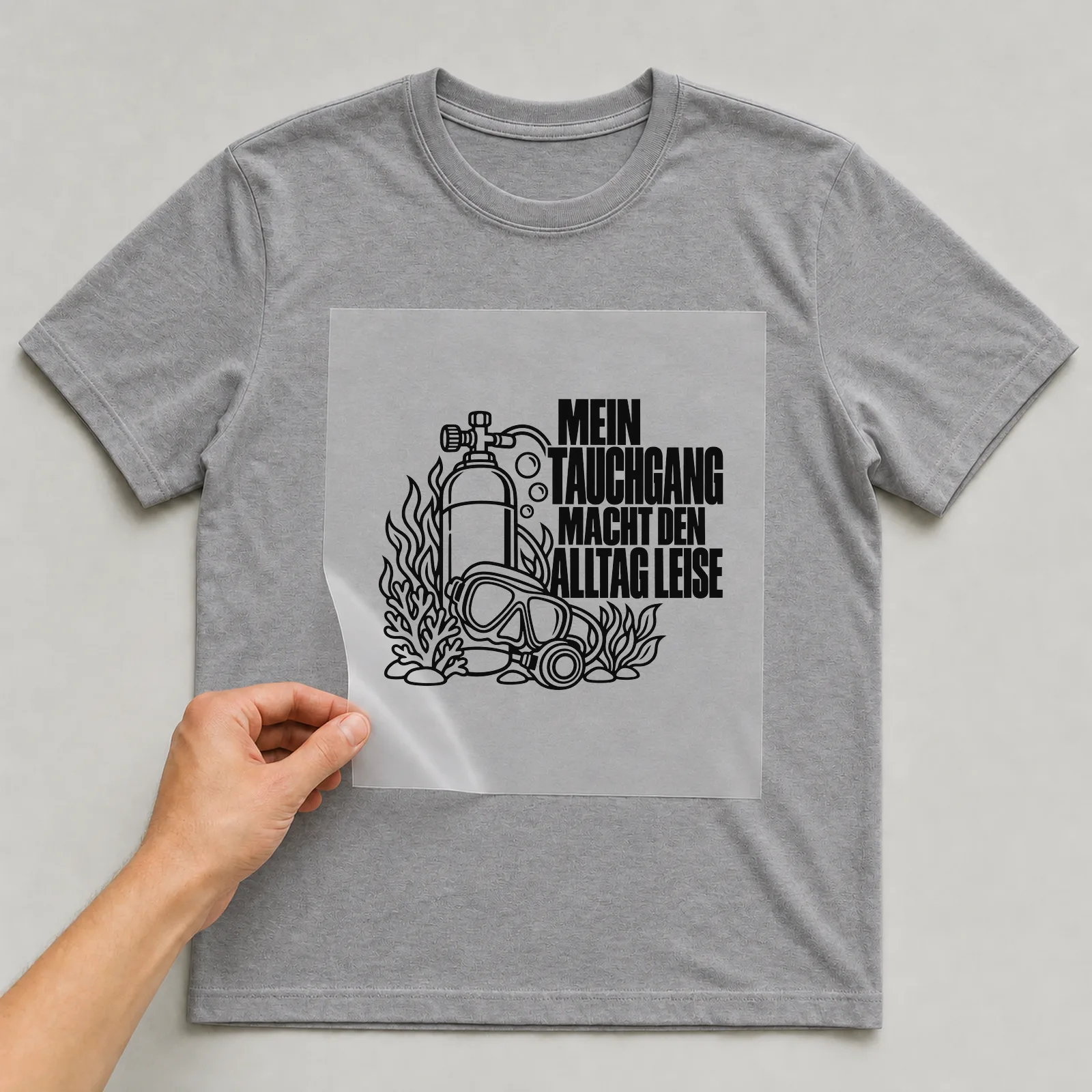 Bügelbild „Mein Tauchgang macht den Alltag leise“ auf grauem T-Shirt, Folie wird aufgelegt