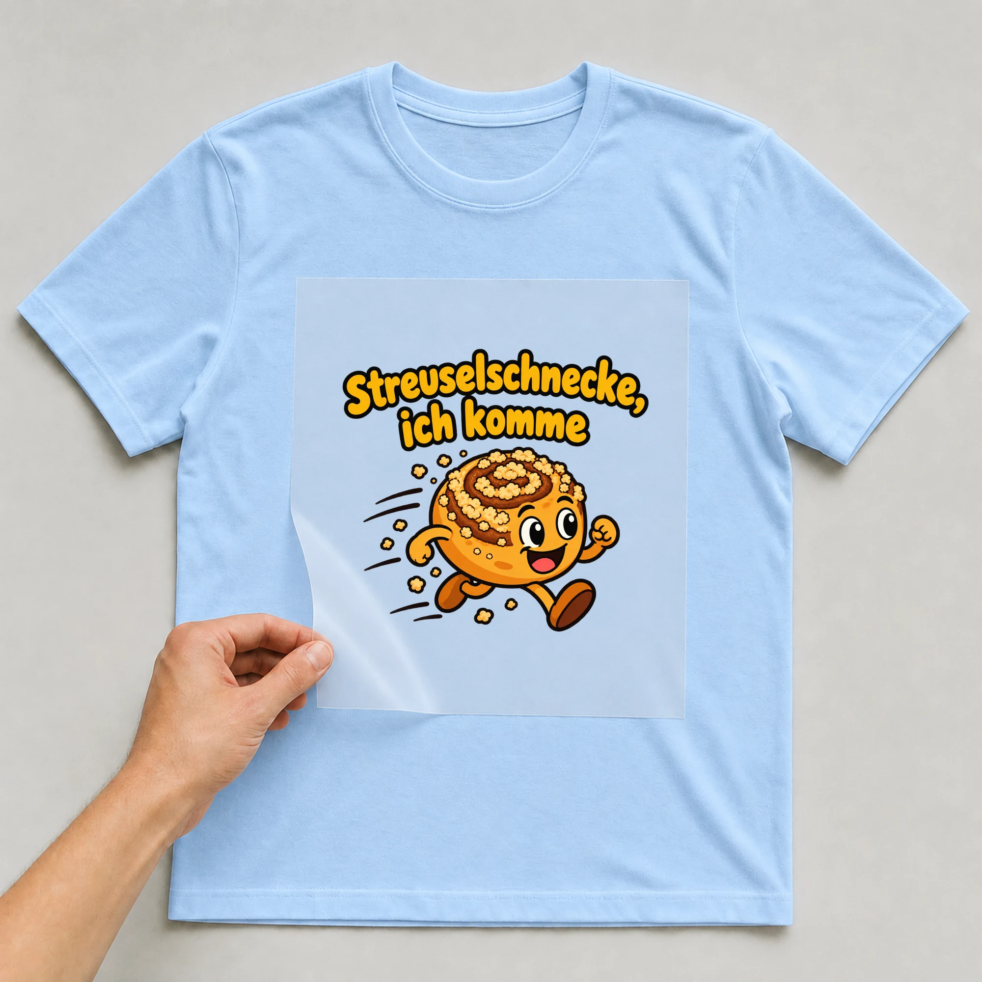 Bügelbild „Streuselschnecke, ich komme“ auf babyblauem T-Shirt, Folie wird aufgelegt