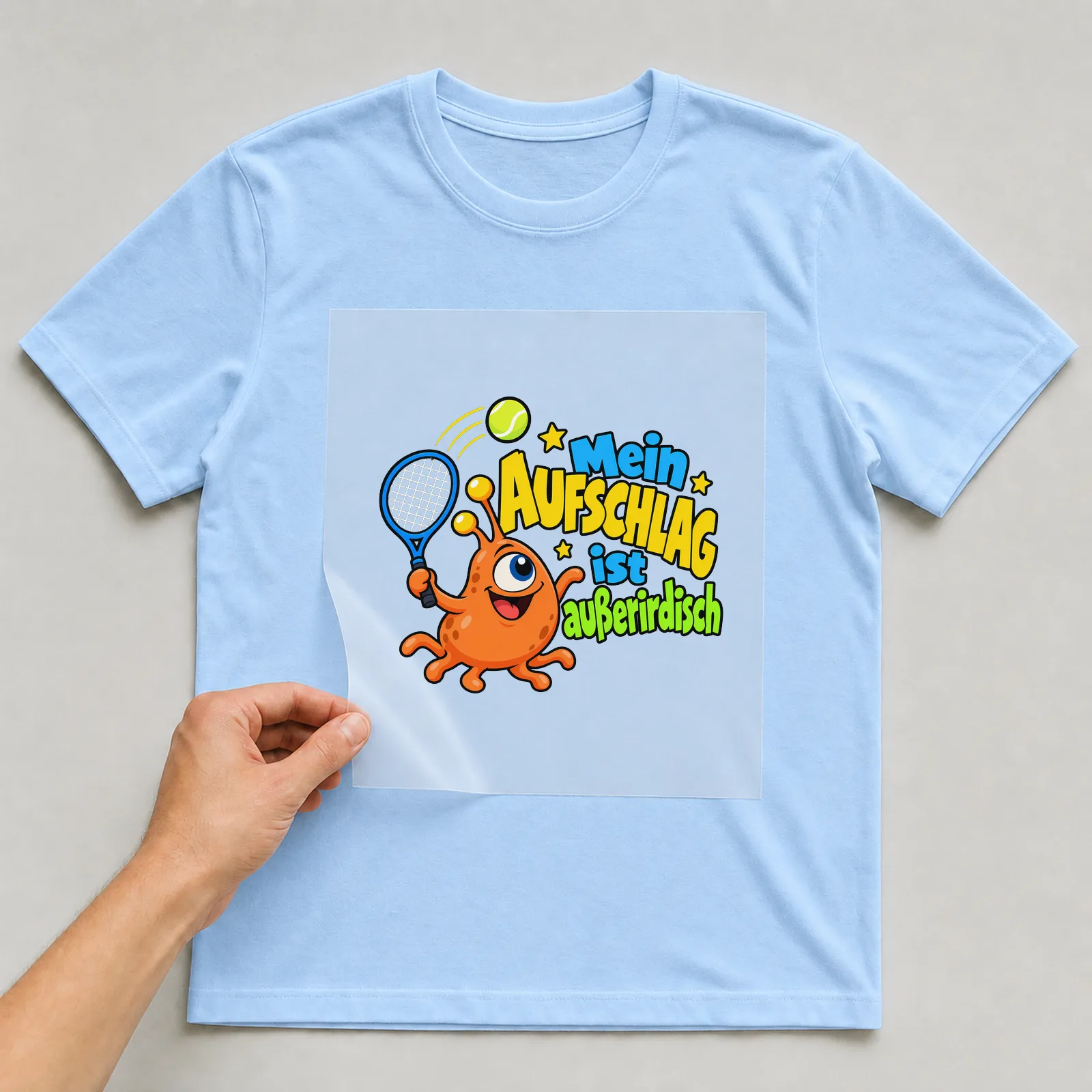 Bügelbild „Mein Aufschlag ist außerirdisch“ auf hellblauem T-Shirt, Folie wird aufgelegt