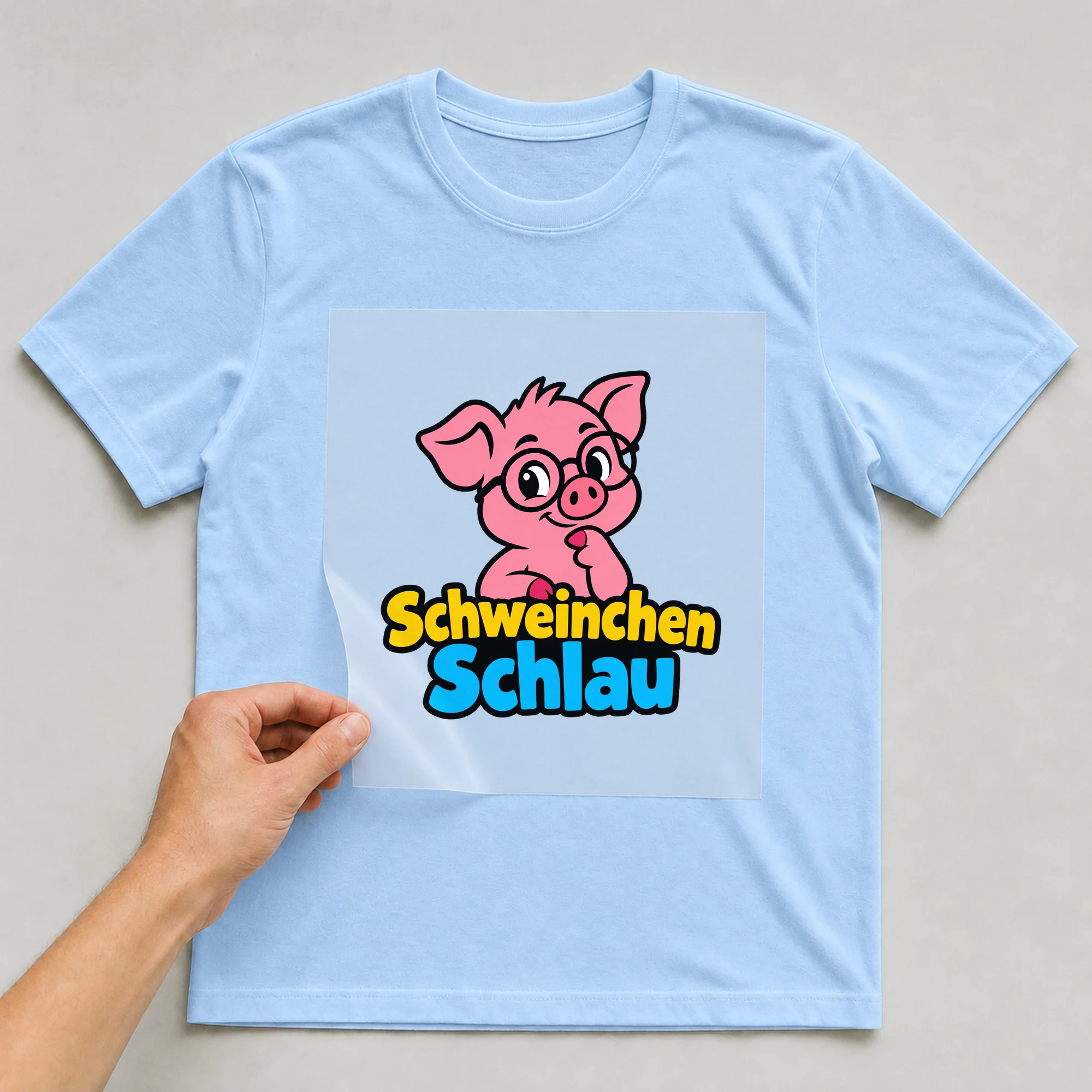 Bügelbild „Schweinchen Schlau“ auf babyblauem T-Shirt, Folie wird aufgelegt