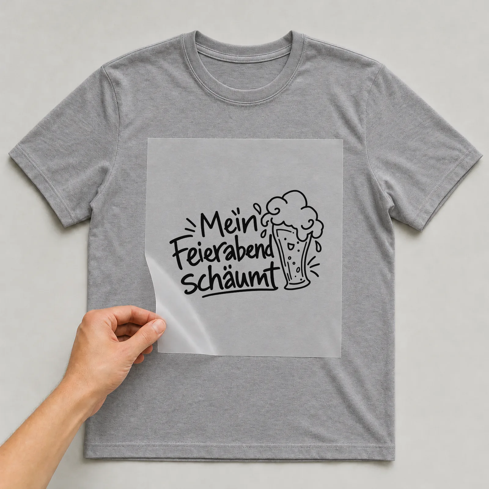 Bügelbild „Mein Feierabend schäumt“ auf grauem T-Shirt, Folie wird aufgelegt