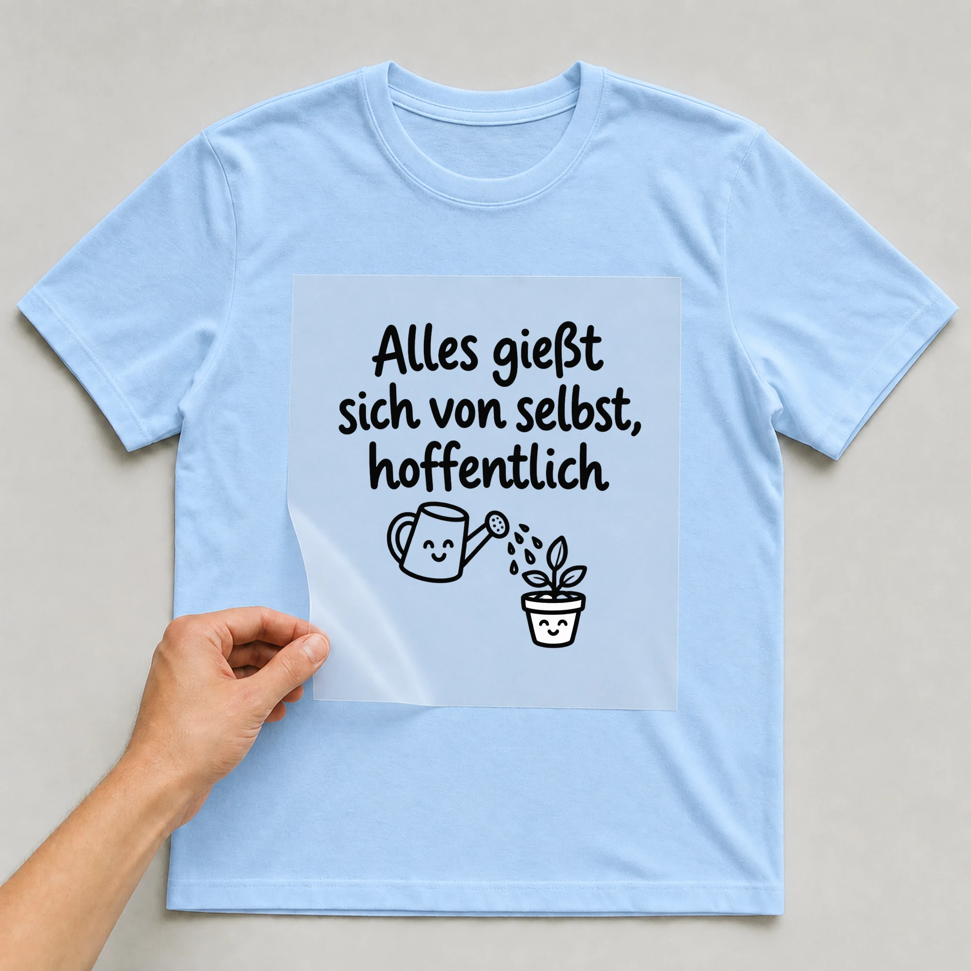 Bügelbild „Alles giesst sich von selbst hoffentlich“ auf babyblauem T-Shirt, Folie wird aufgelegt