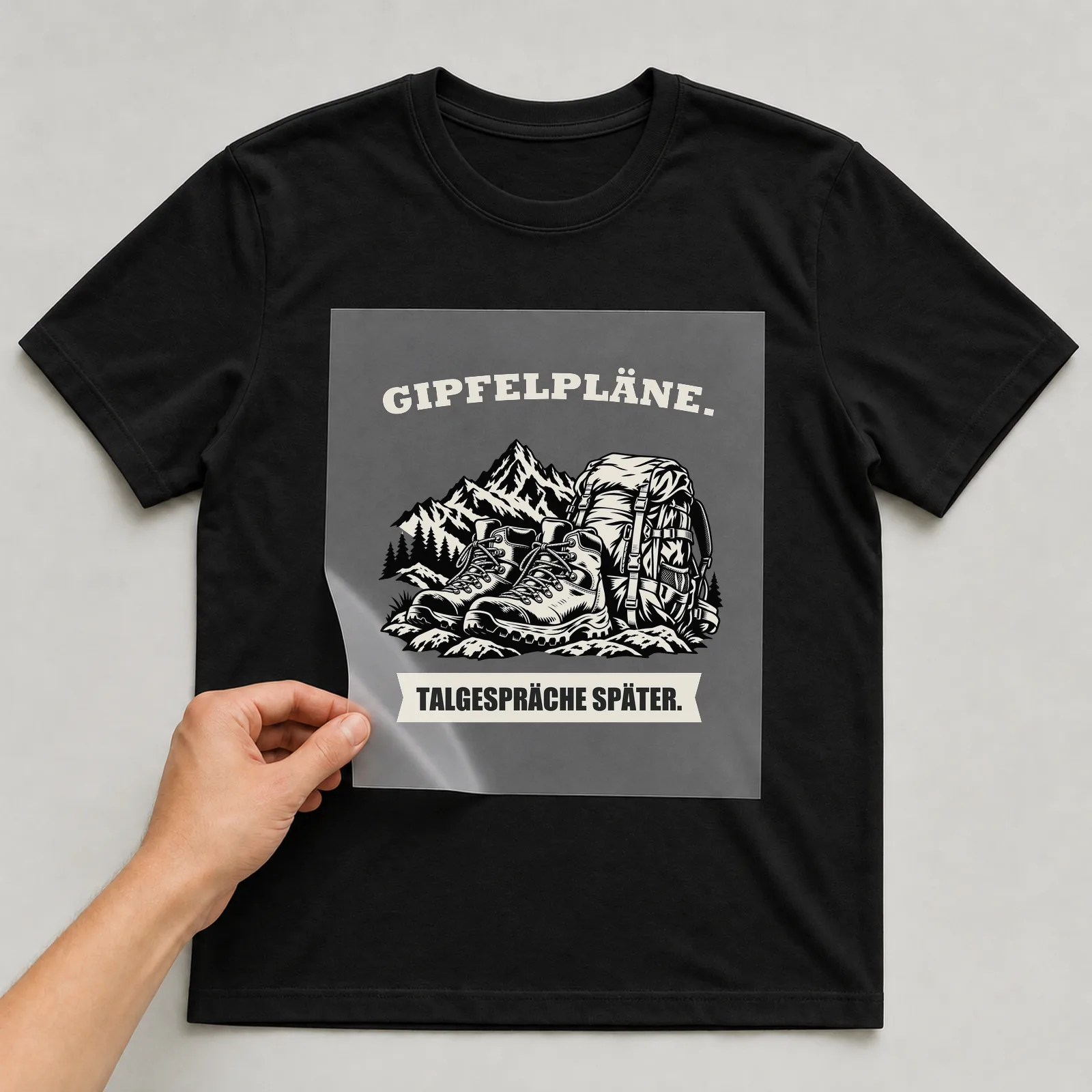 Bügelbild „Gipfelpläne. Talgespräche Später.“ auf schwarzem T-Shirt, Folie wird aufgelegt