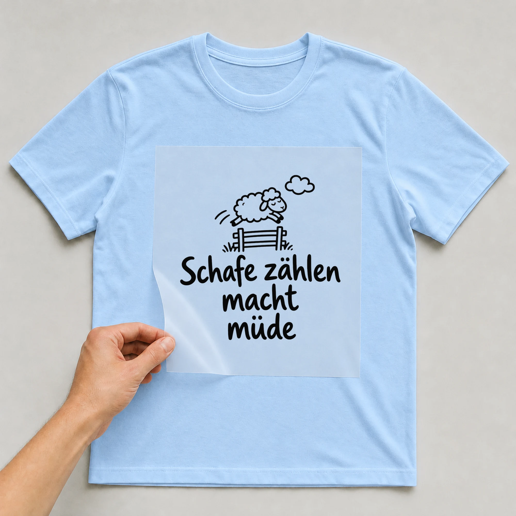 Bügelbild „Schafe zählen macht müde“ auf babyblauem T-Shirt, Folie wird aufgelegt