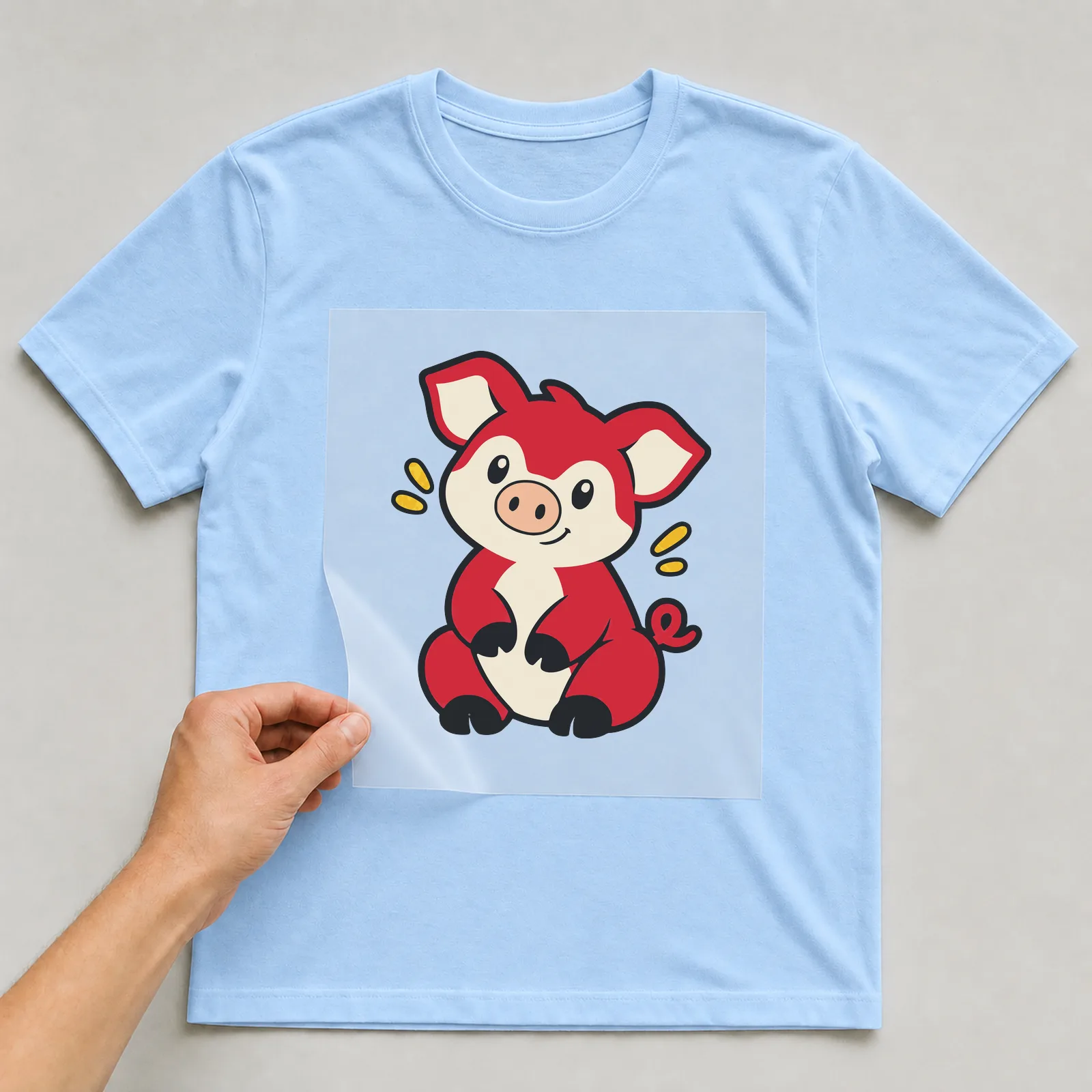 Bügelbild Schwein im Comic-Stil auf hellblauem T-Shirt, Folie wird aufgelegt