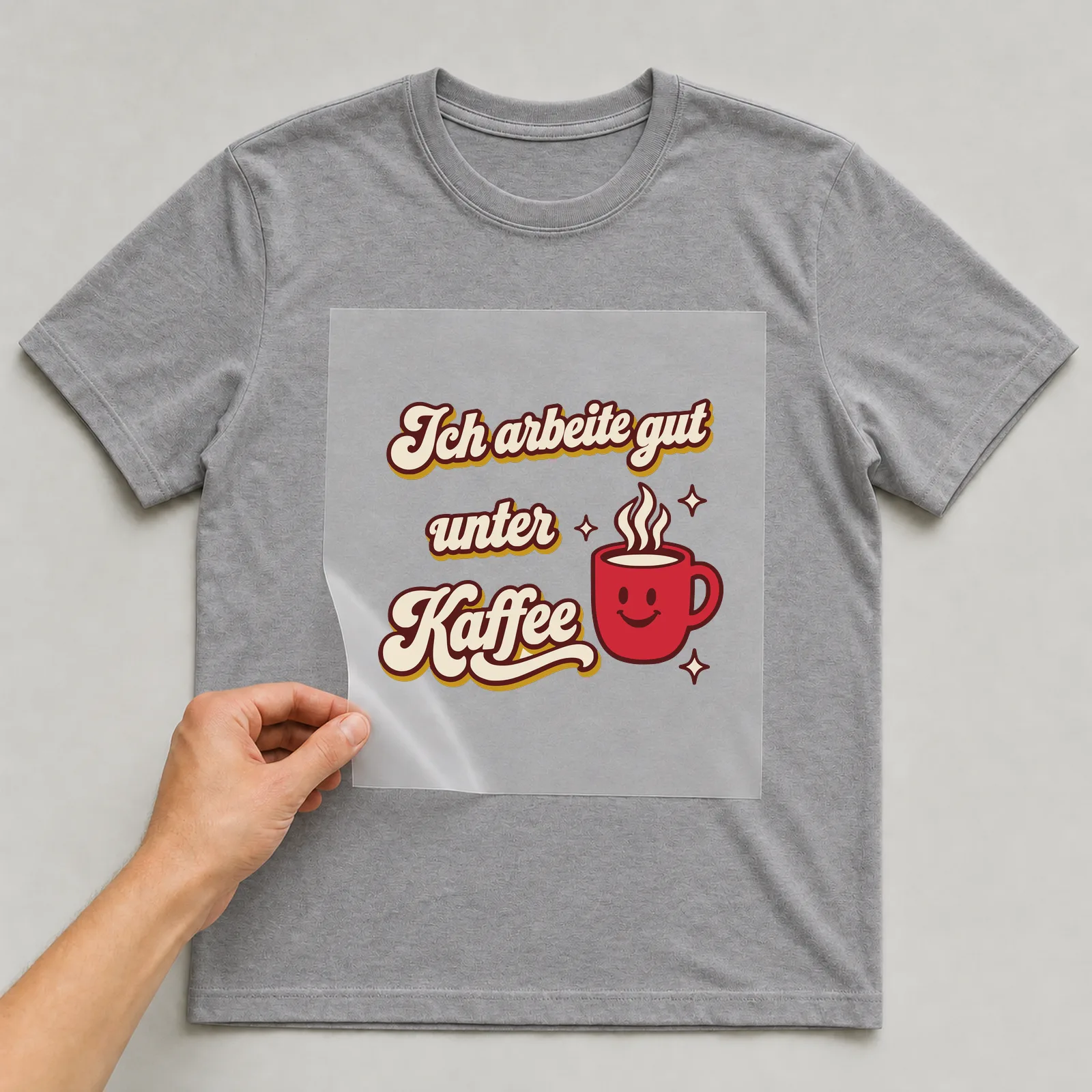 Bügelbild Ich arbeite gut unter Kaffee auf grauem T-Shirt, Folie wird aufgelegt