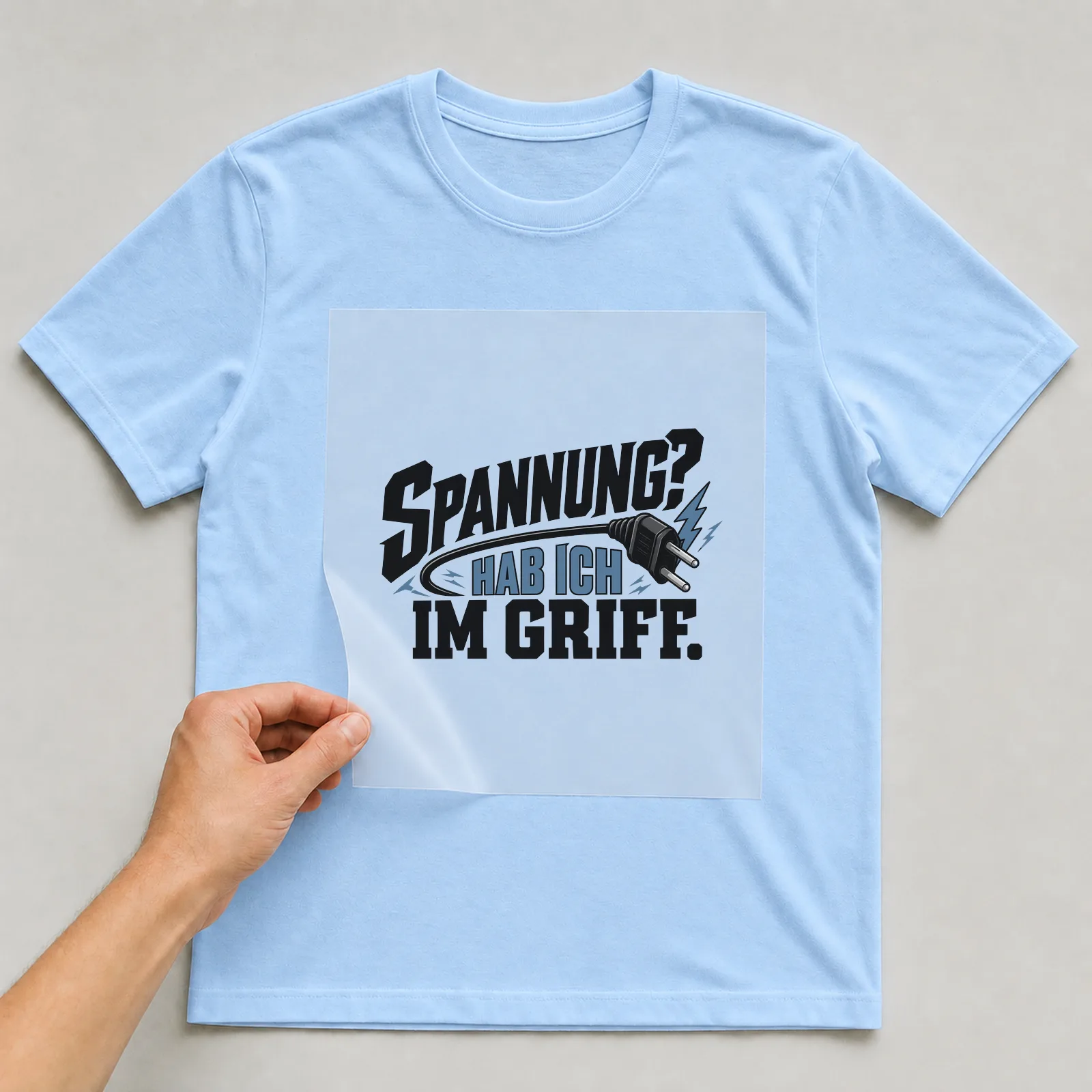 Bügelbild „Spannung? Hab ich im Griff.“ auf hellblauem T-Shirt, Folie wird aufgelegt