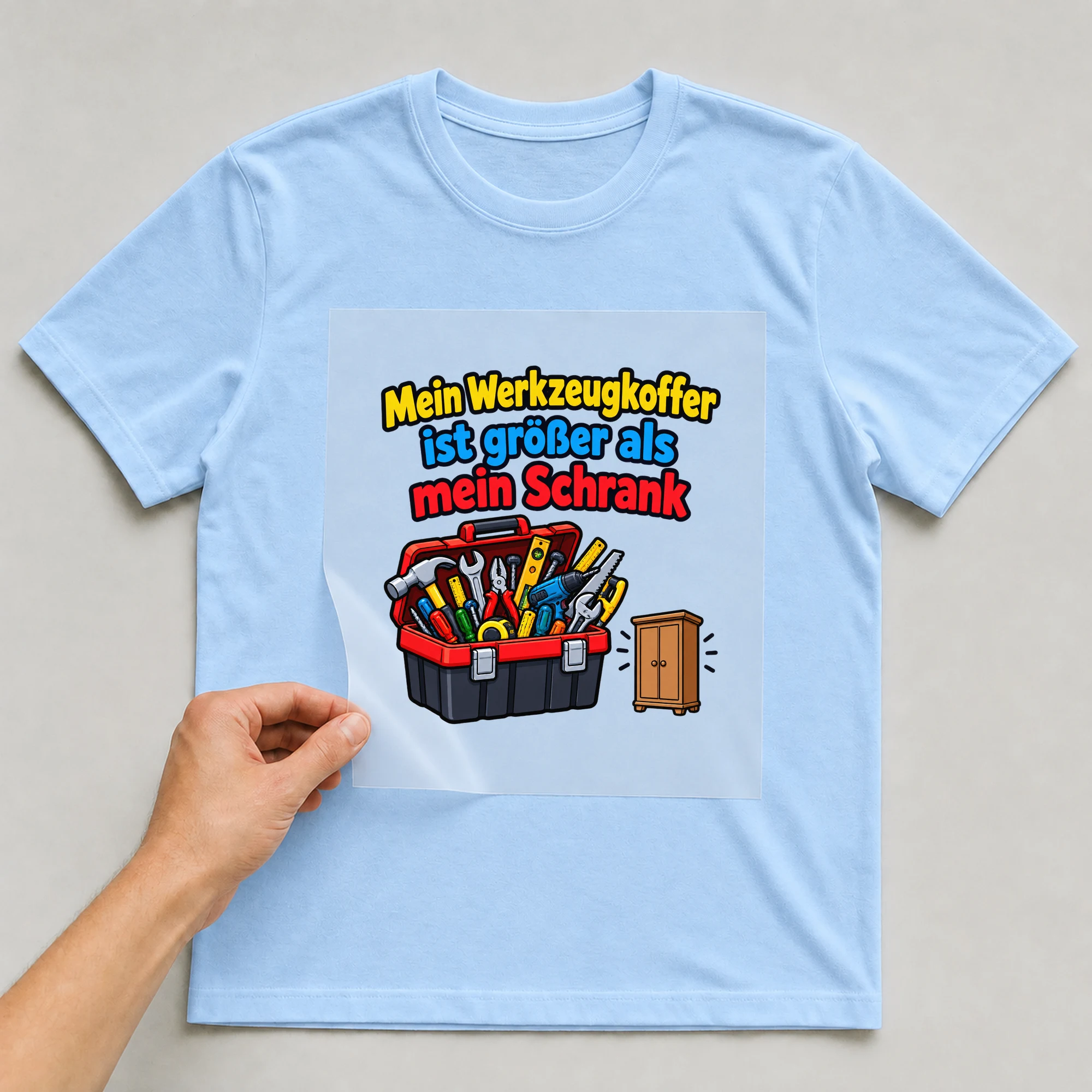 Bügelbild „Mein Werkzeugkoffer ist größer als mein Schrank“ auf babyblauem T-Shirt, Folie wird aufgelegt