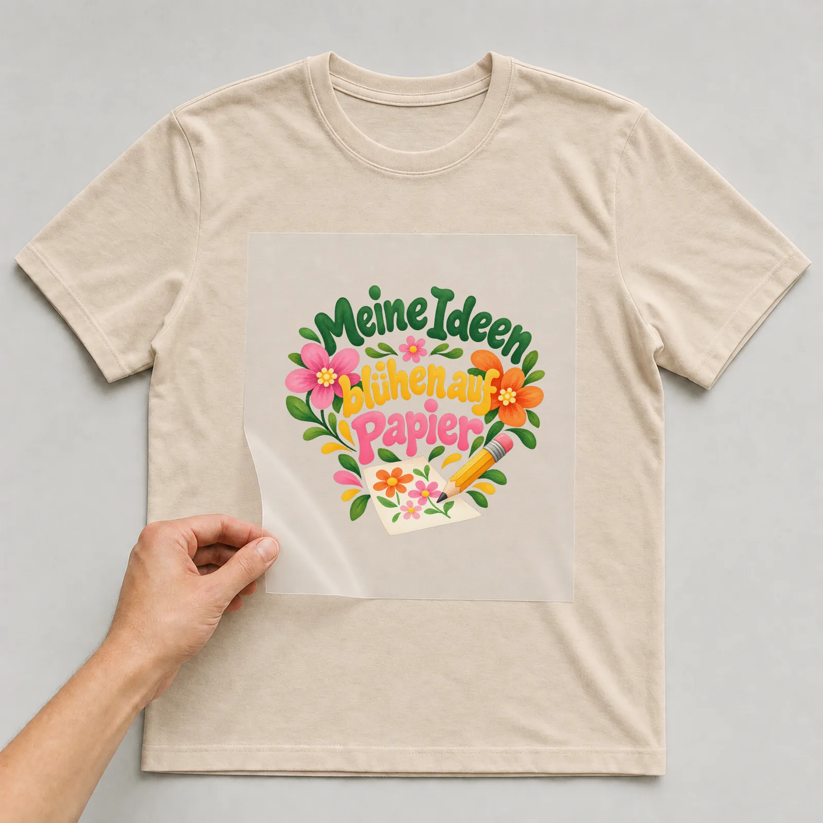 Bügelbild „Meine Ideen blühen auf Papier“ auf beigem T-Shirt, Folie wird aufgelegt