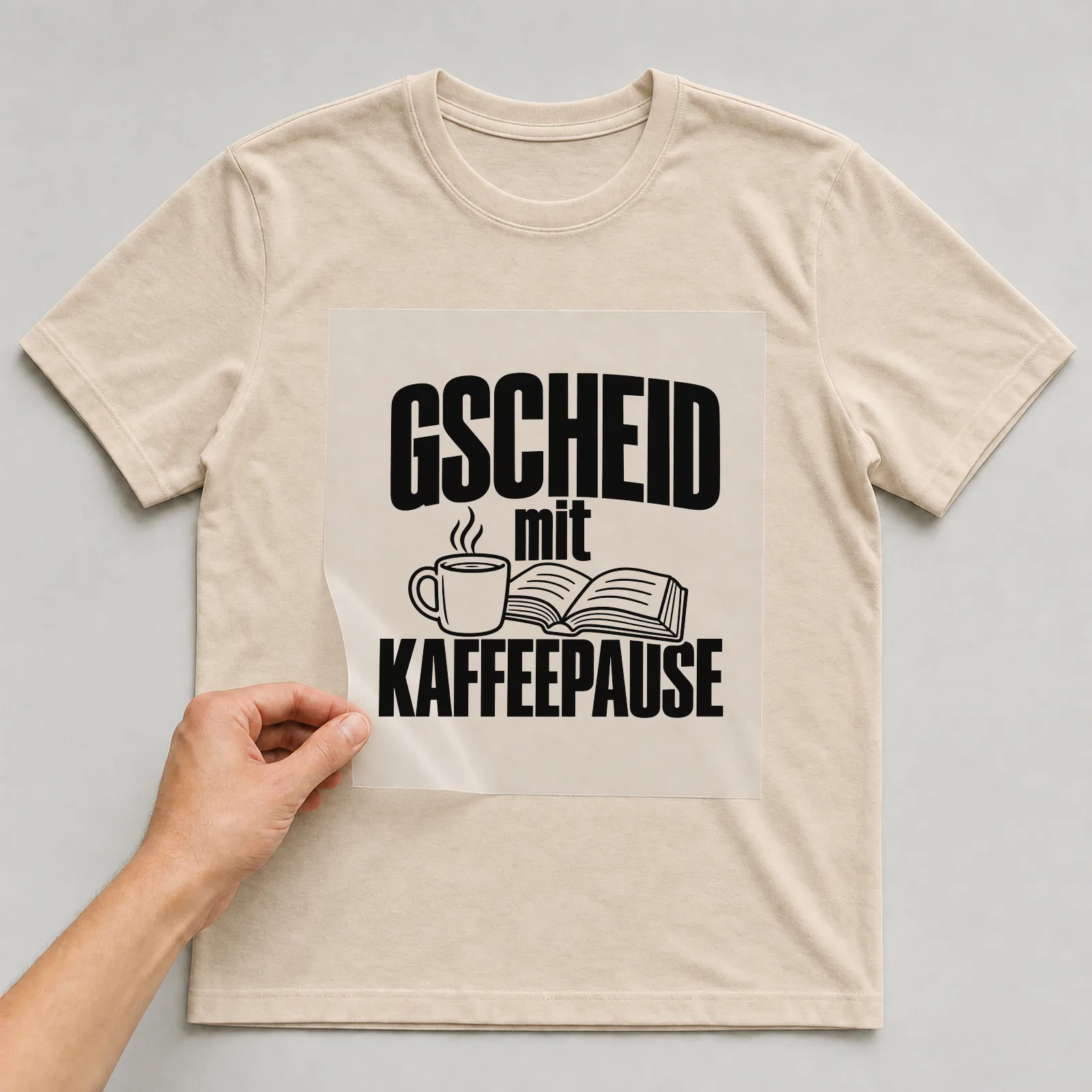 Bügelbild „Gscheid mit Kaffeepause“ auf beigem T-Shirt, Folie wird aufgelegt