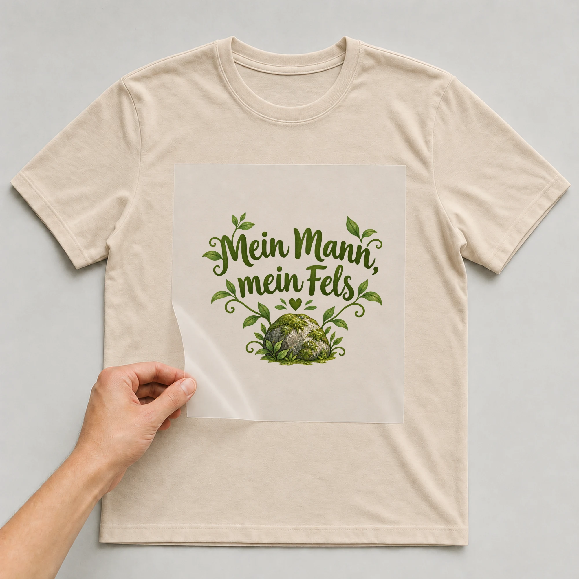 Bügelbild „Mein Mann, mein Fels“ auf beigem T-Shirt, Folie wird aufgelegt