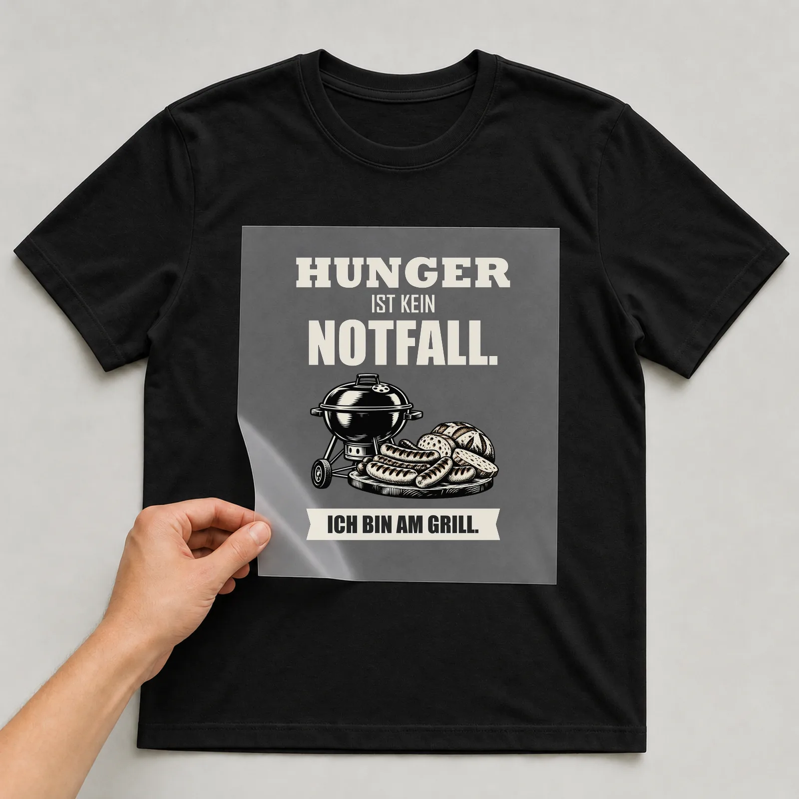 Bügelbild „Hunger ist kein Notfall. Ich bin am Grill.“ auf schwarzem T-Shirt, Folie wird aufgelegt