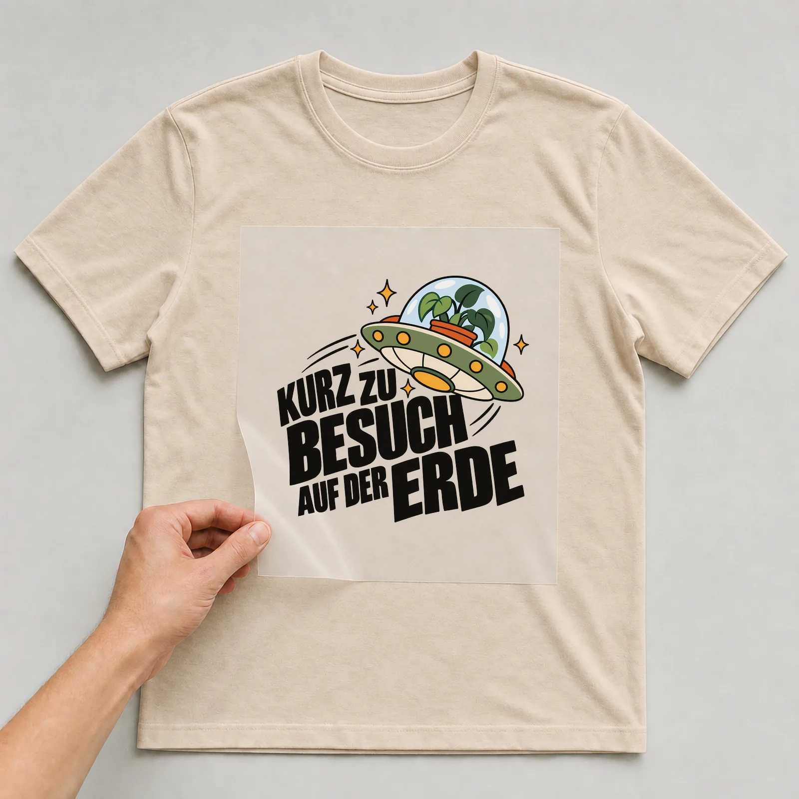 Bügelbild „Kurz zu Besuch auf der Erde“ auf beigem T-Shirt, Folie wird aufgelegt