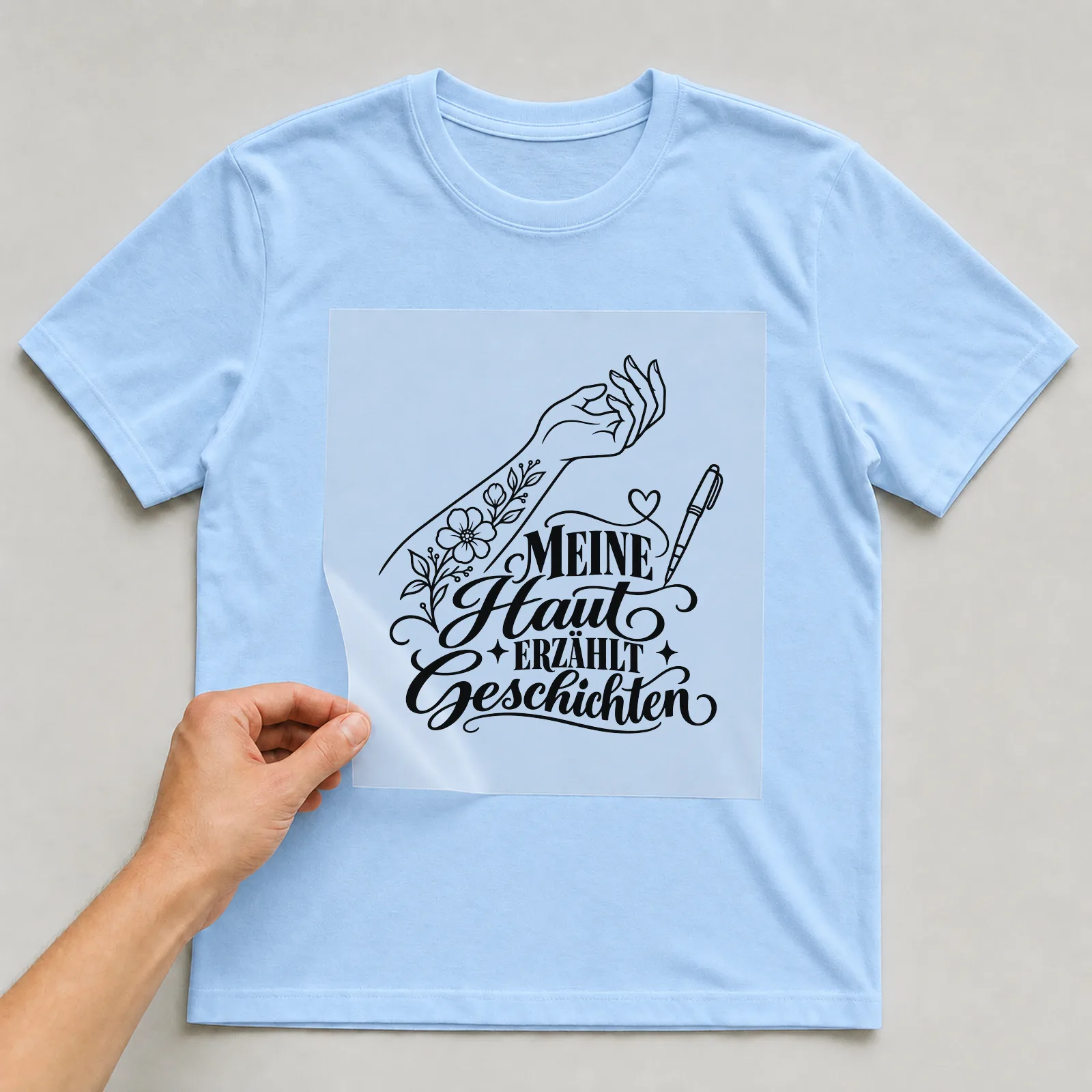 Bügelbild „MEINE Haut ERZÄHLT Geschichten“ auf hellblauem T-Shirt, Folie wird aufgelegt