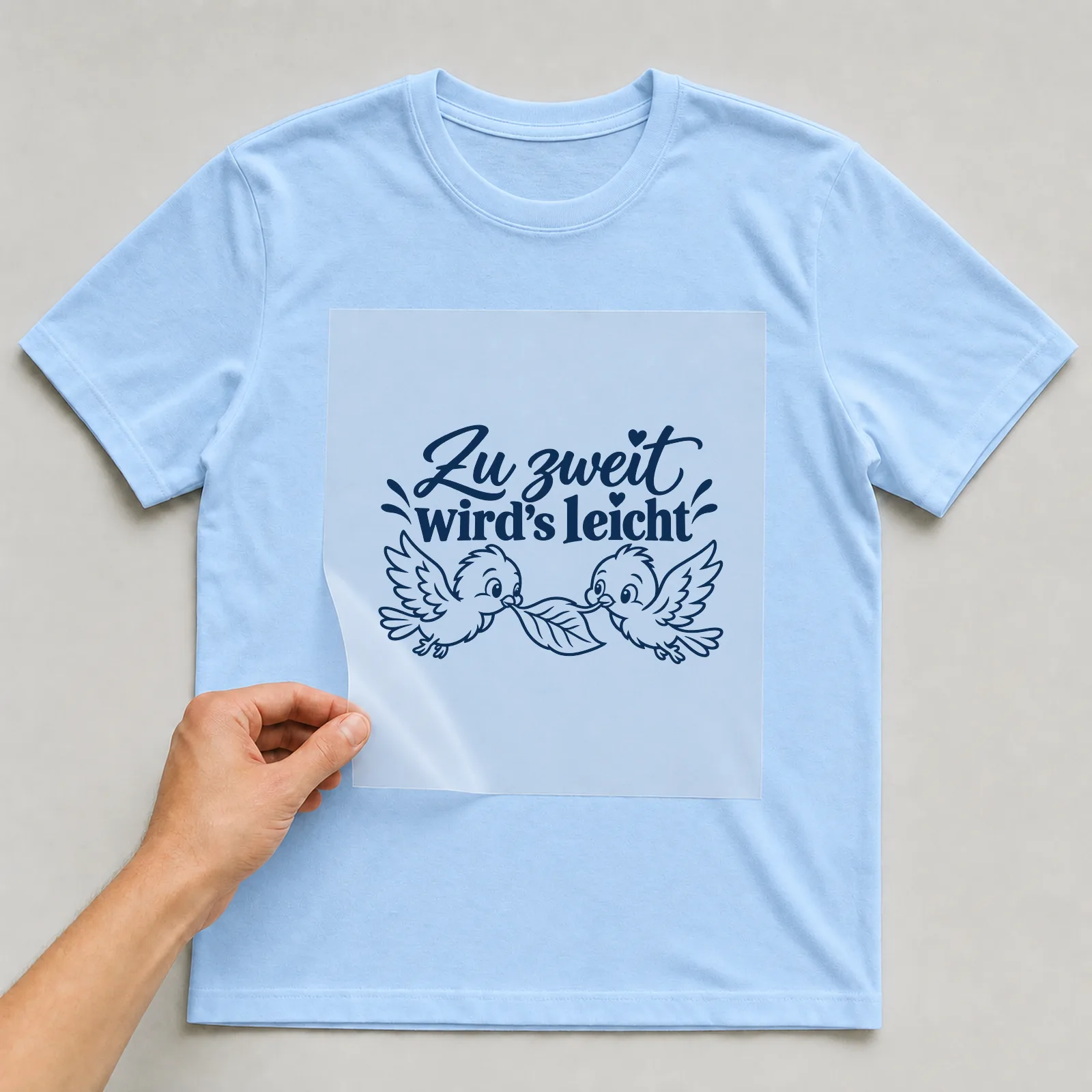 Bügelbild „Zu zweit wird’s leicht“ auf hellblauem T-Shirt, Folie wird aufgelegt