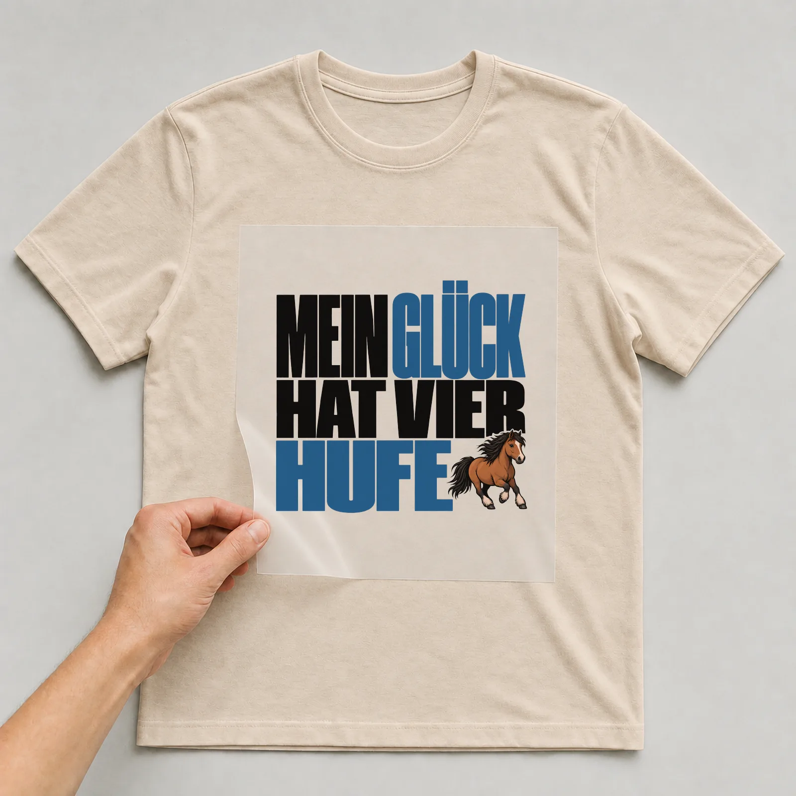 Bügelbild „Mein Glück hat vier Hufe“ auf beigem T-Shirt, Folie wird aufgelegt