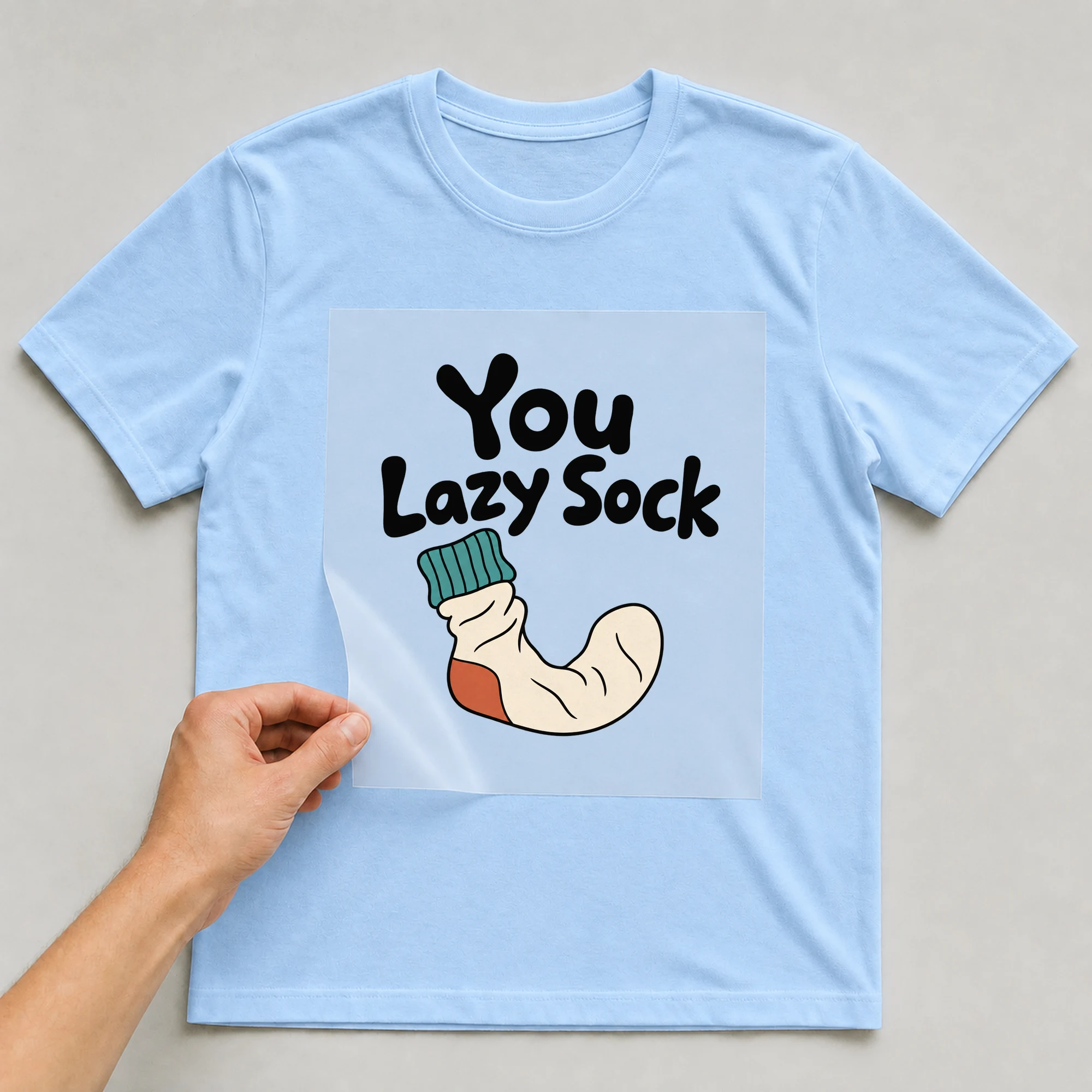 Bügelbild „You Lazy Sock“ auf babyblauem T-Shirt, Folie wird aufgelegt