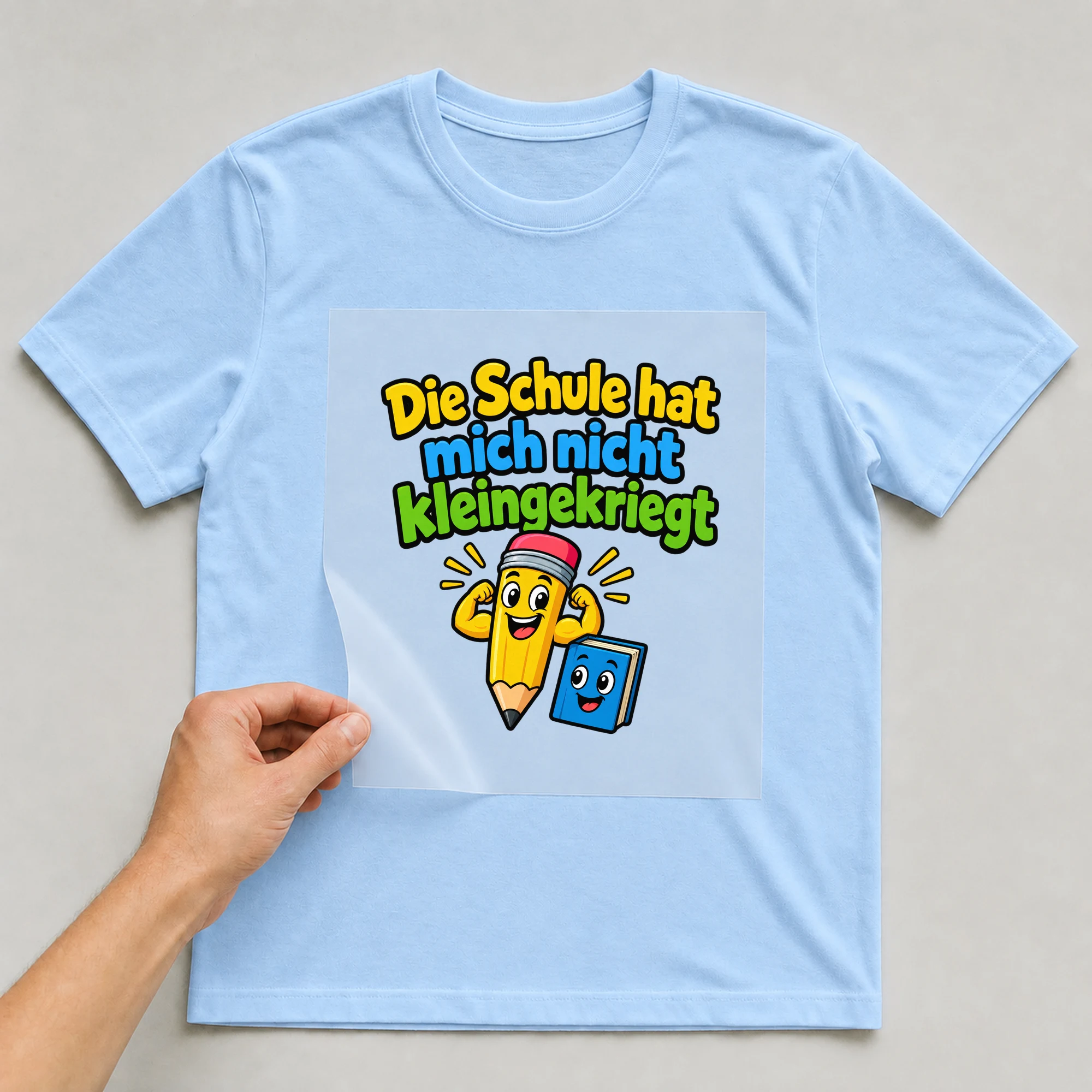 Bügelbild „Die schule hat mich nicht kleingekriegt“ auf babyblauem T-Shirt, Folie wird aufgelegt