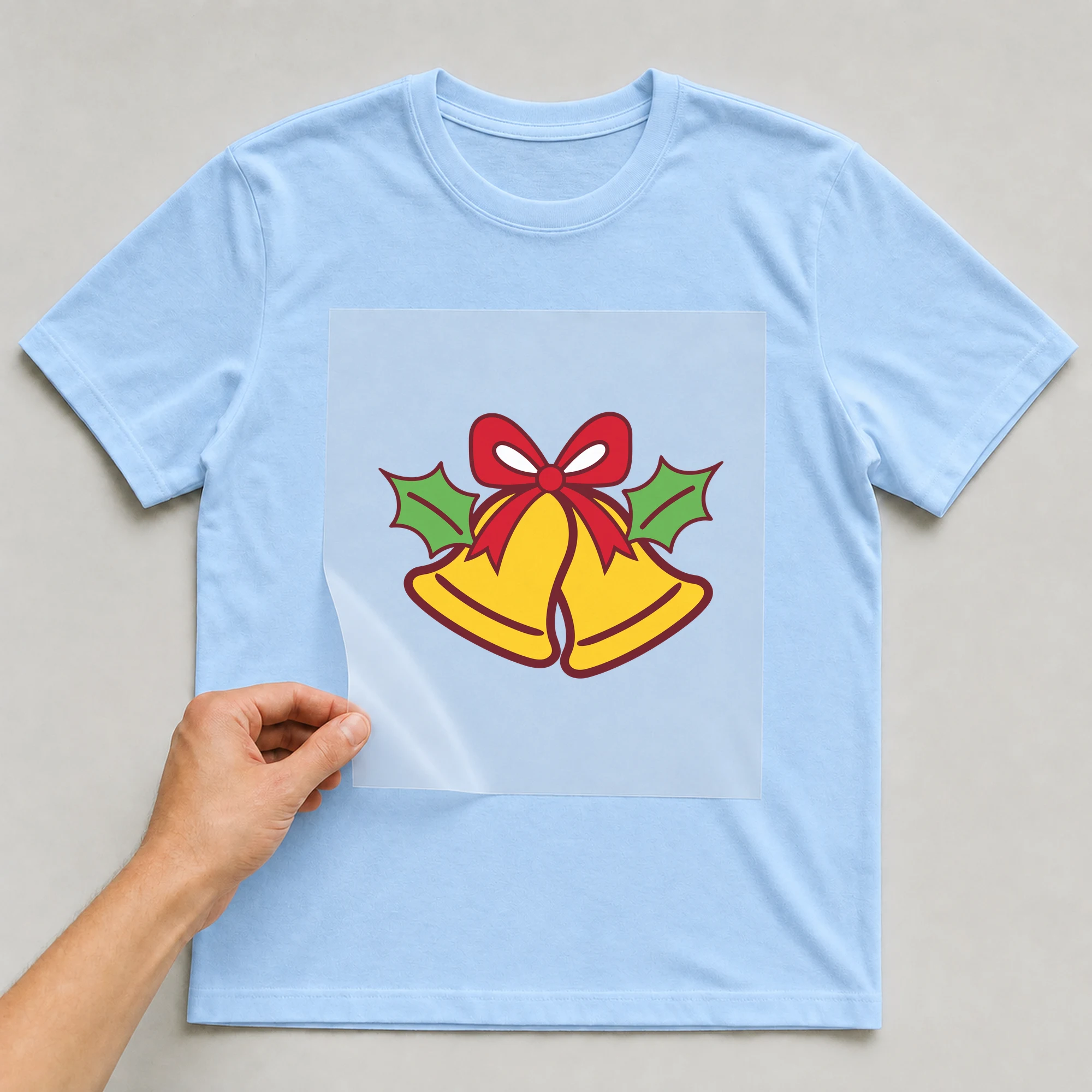 Bügelbild „Glöckchen“ auf babyblauem T-Shirt, Folie wird aufgelegt
