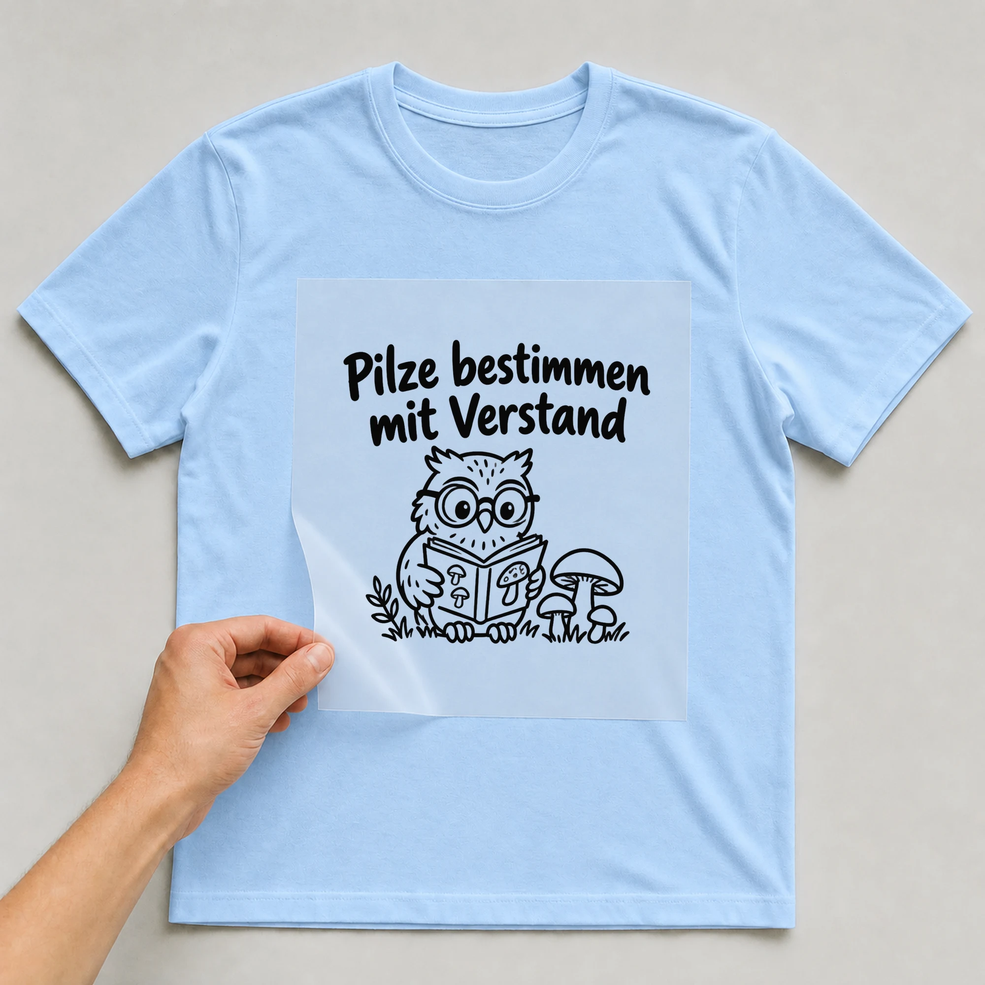Bügelbild „Pilze bestimmen mit Verstand“ auf babyblauem T-Shirt, Folie wird aufgelegt