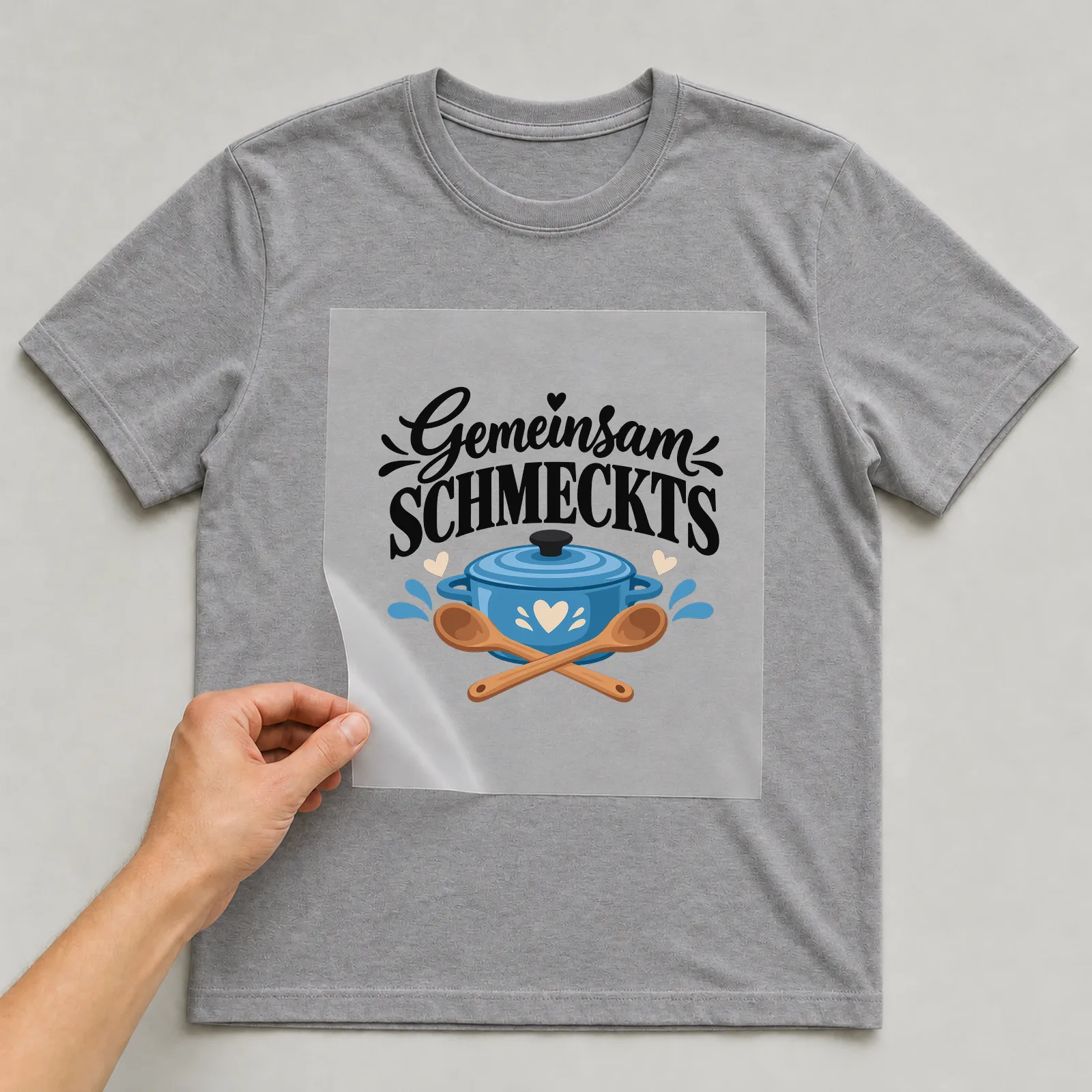 Bügelbild „Gemeinsam schmeckt’s“ auf grauem T-Shirt, Folie wird aufgelegt