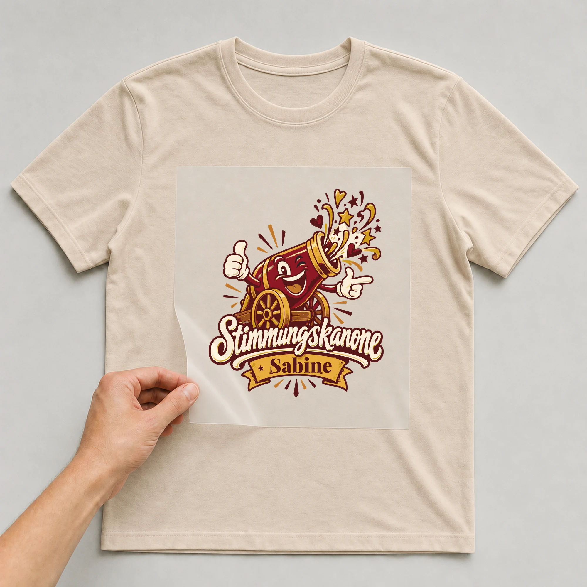 Bügelbild Stimmungskanone mit Name auf beigem T-Shirt, Folie wird aufgelegt