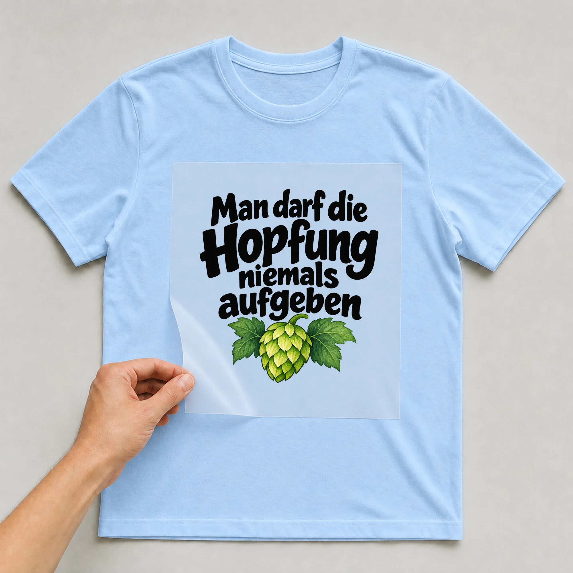 Bügelbild „Man darf die Hopfung niemals aufgeben“ auf babyblauem T-Shirt, Folie wird aufgelegt